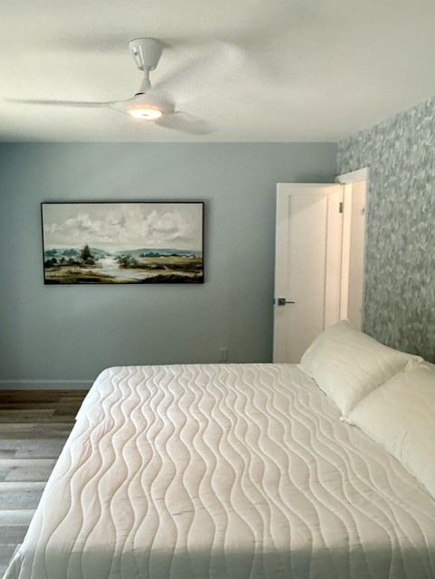 Bedroom with a bed, a painting on the wall, and a ceiling fan, door slightly open, light-colored walls.