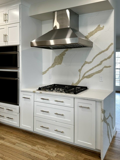 Kitchen with white cabinets, a stainless steel range hood, and a marble backsplash with gold veining.