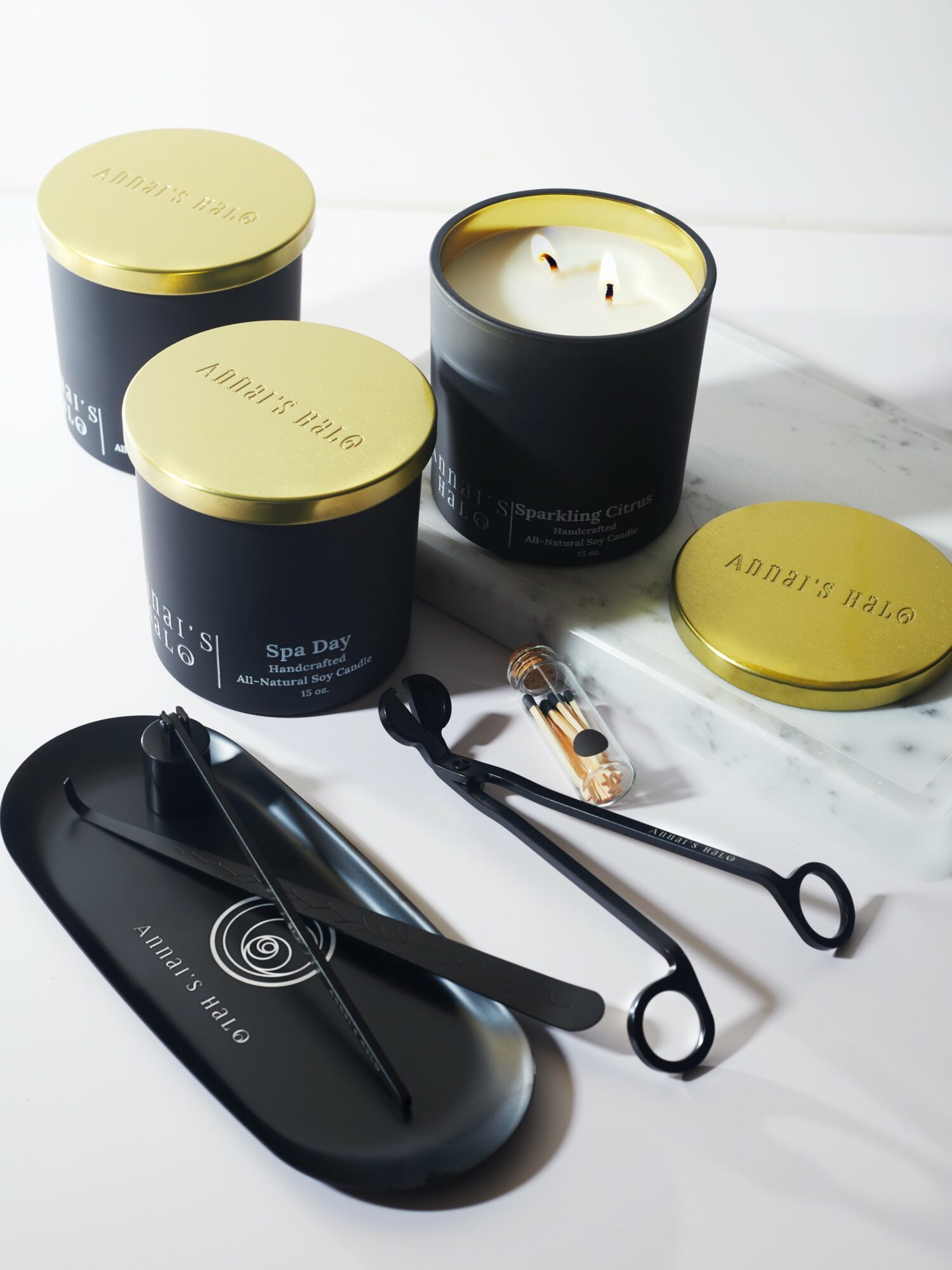 Three black candles with gold lids, a black facial roller, and a black device on a white surface.