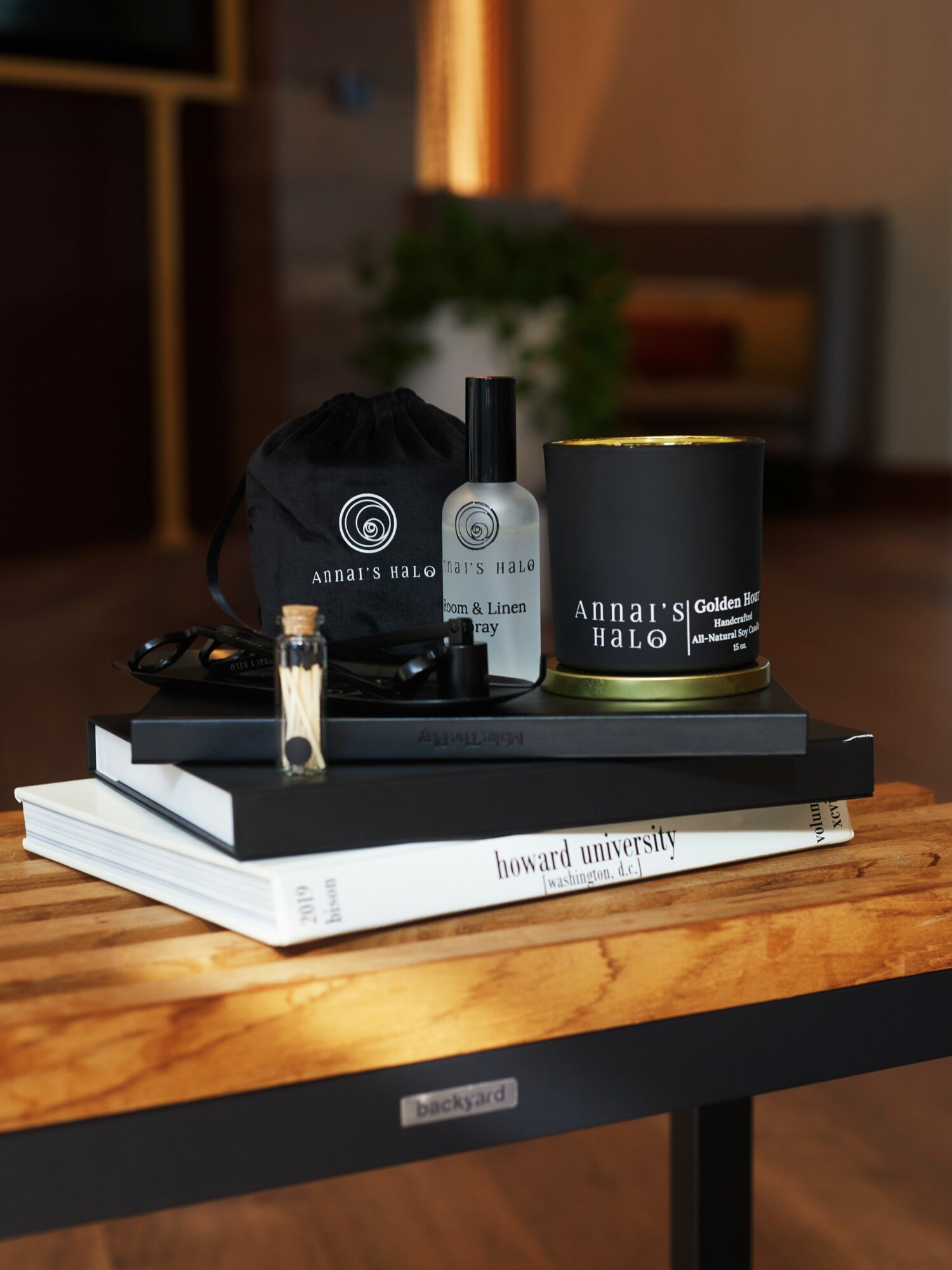 Stack of books with black and white items, a small bottle, and a candle on a wooden table, background blurred.