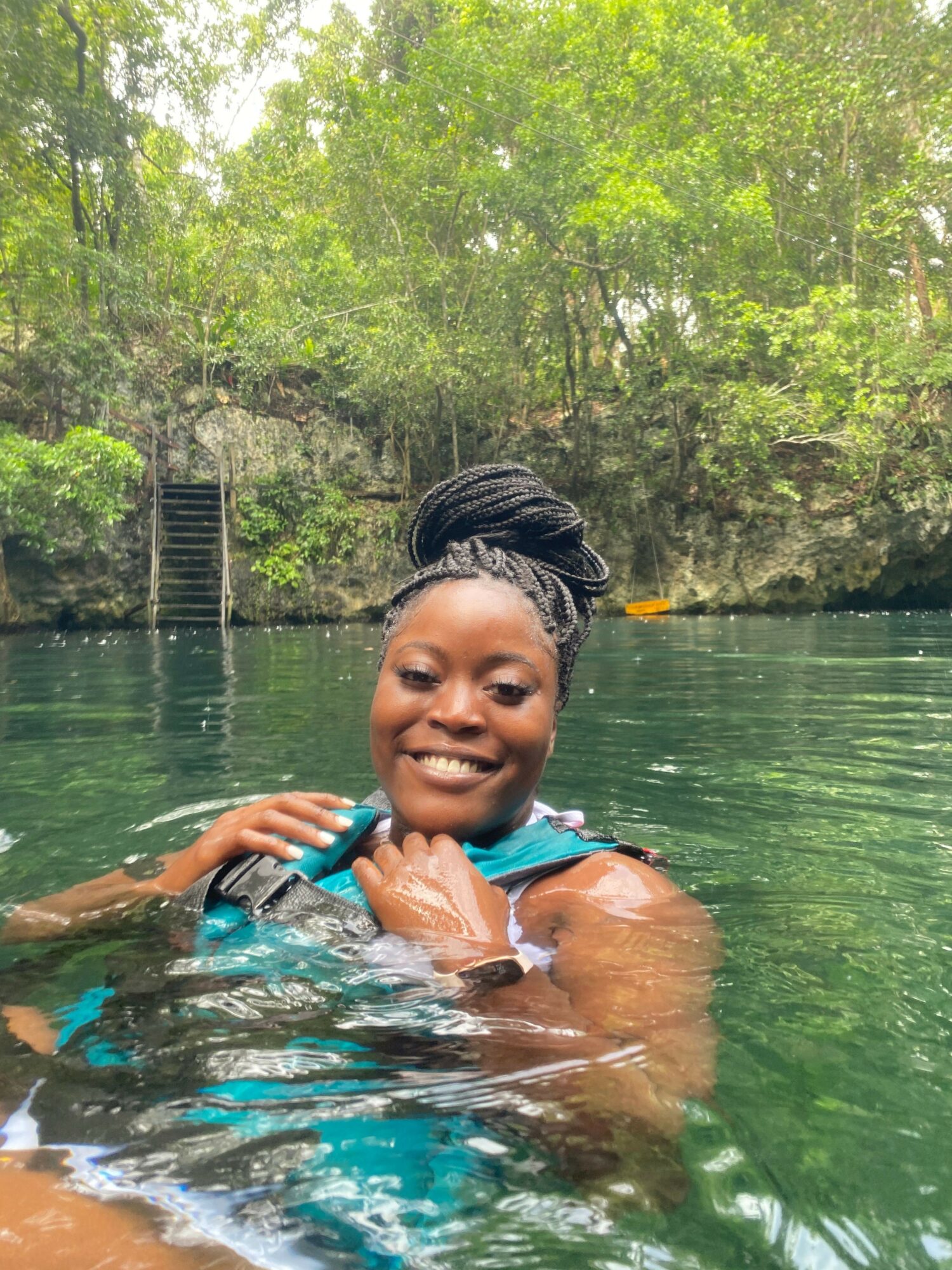 Young woman swimming in a pool with trees in the background, smiling and holding a pool float.