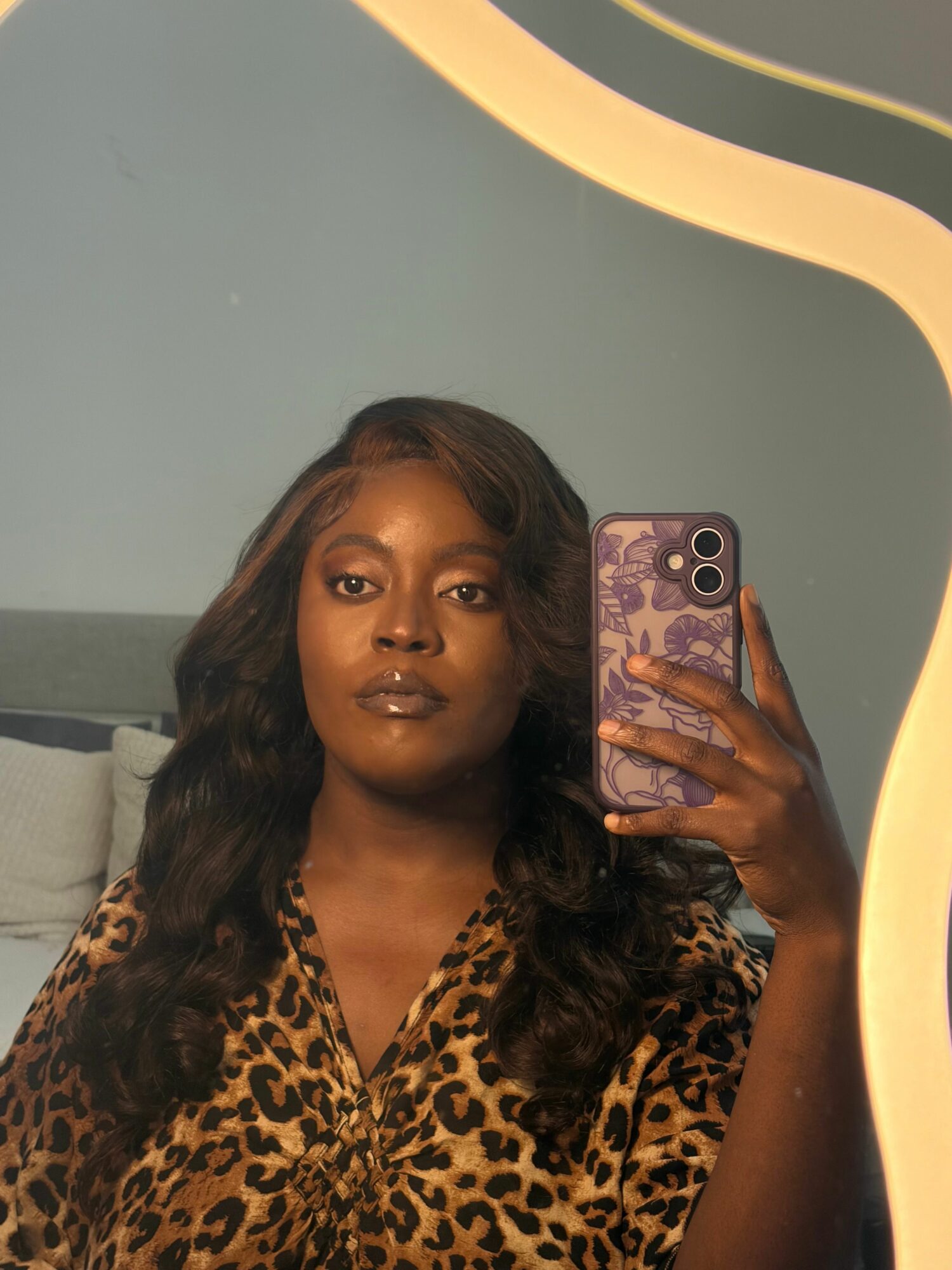 Woman with long dark hair taking a mirror selfie, wearing a leopard print top, holding a phone with a patterned case.