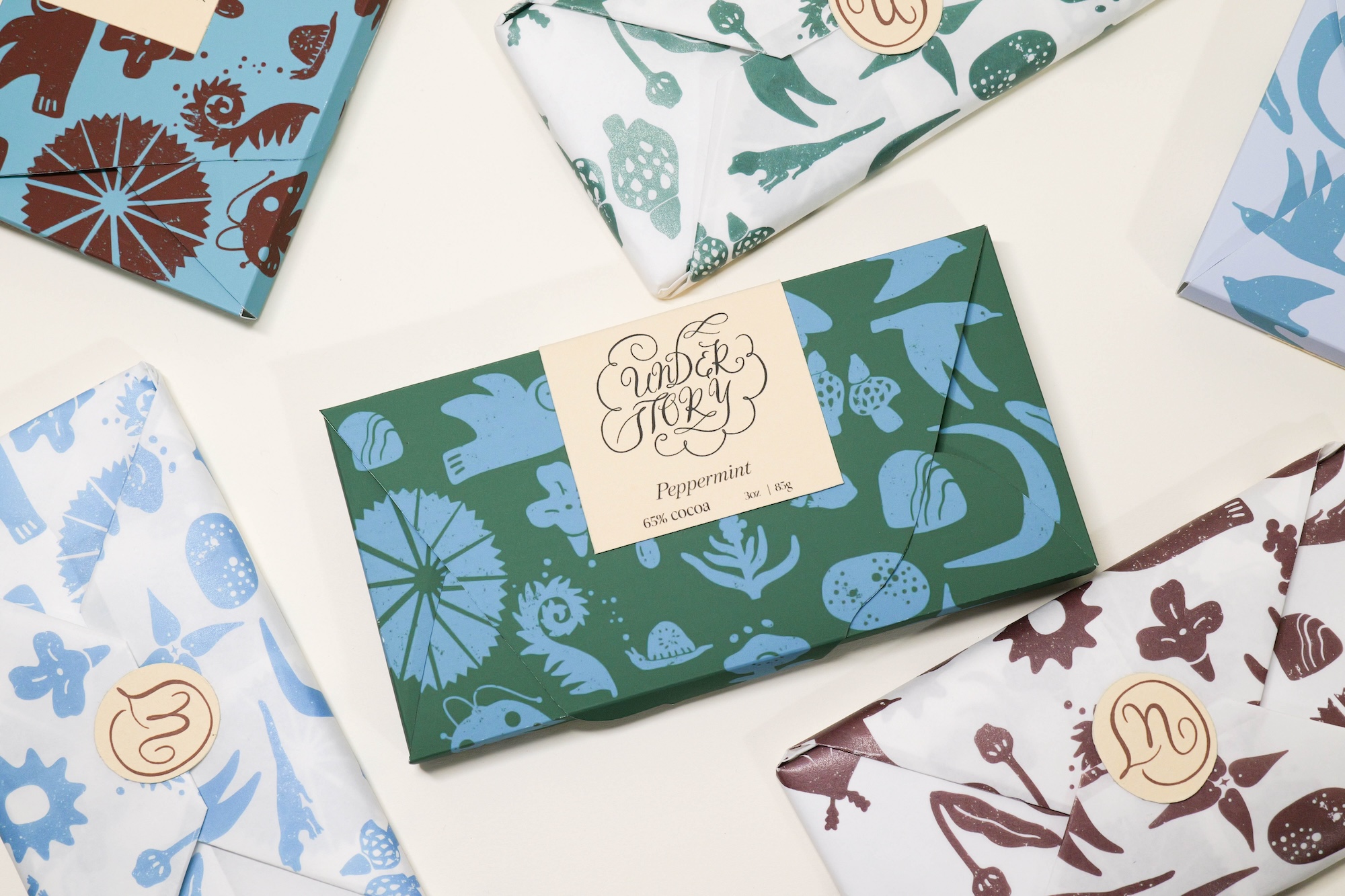 Flat layout of various wrapped gift boxes with nature-themed patterns in blue, green, and brown colors, some with gold logos.