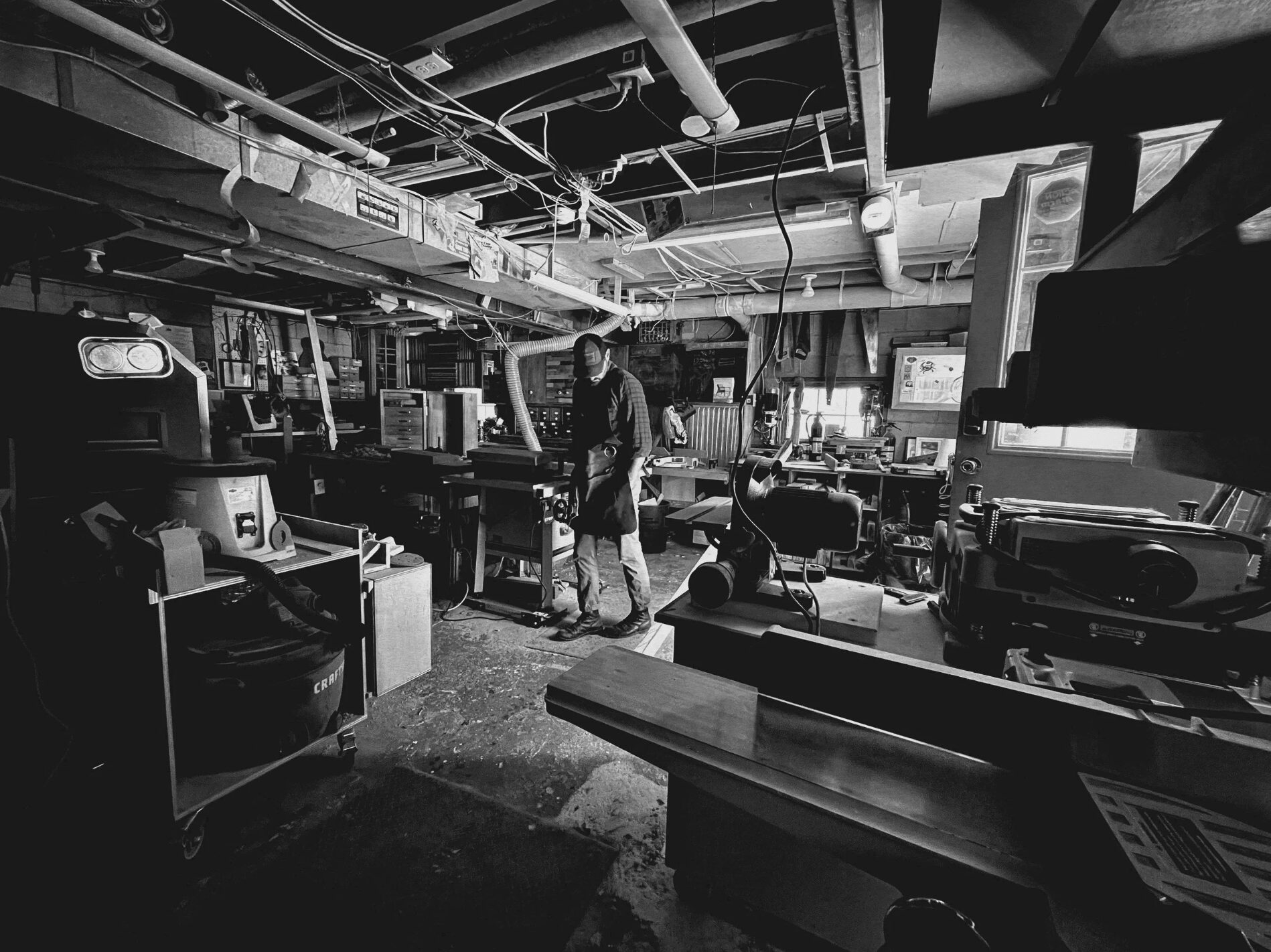 Person standing in a cluttered workshop or laboratory with various equipment and machinery around.