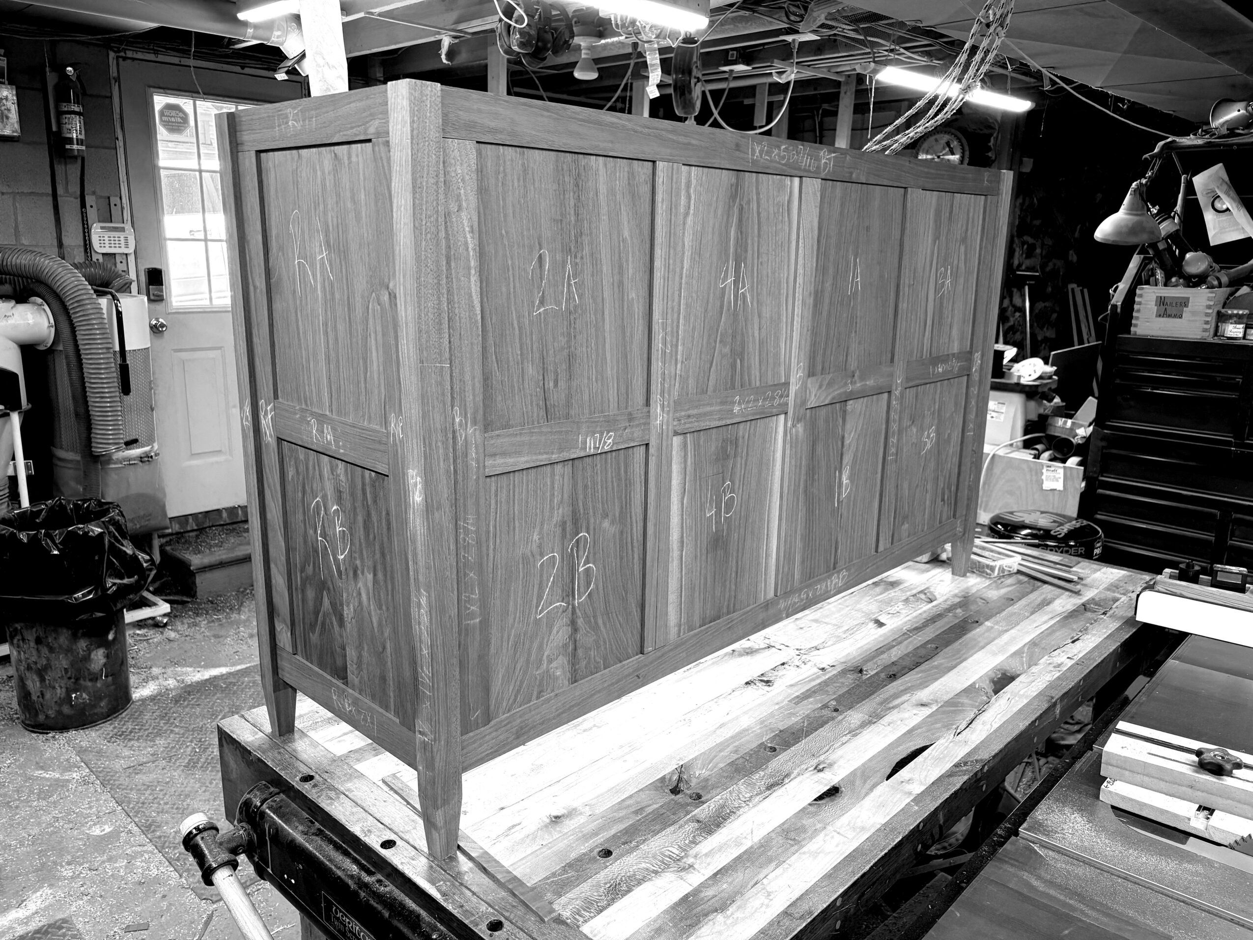 Wooden cabinet on a workbench in a workshop, with tools and equipment visible in the background.