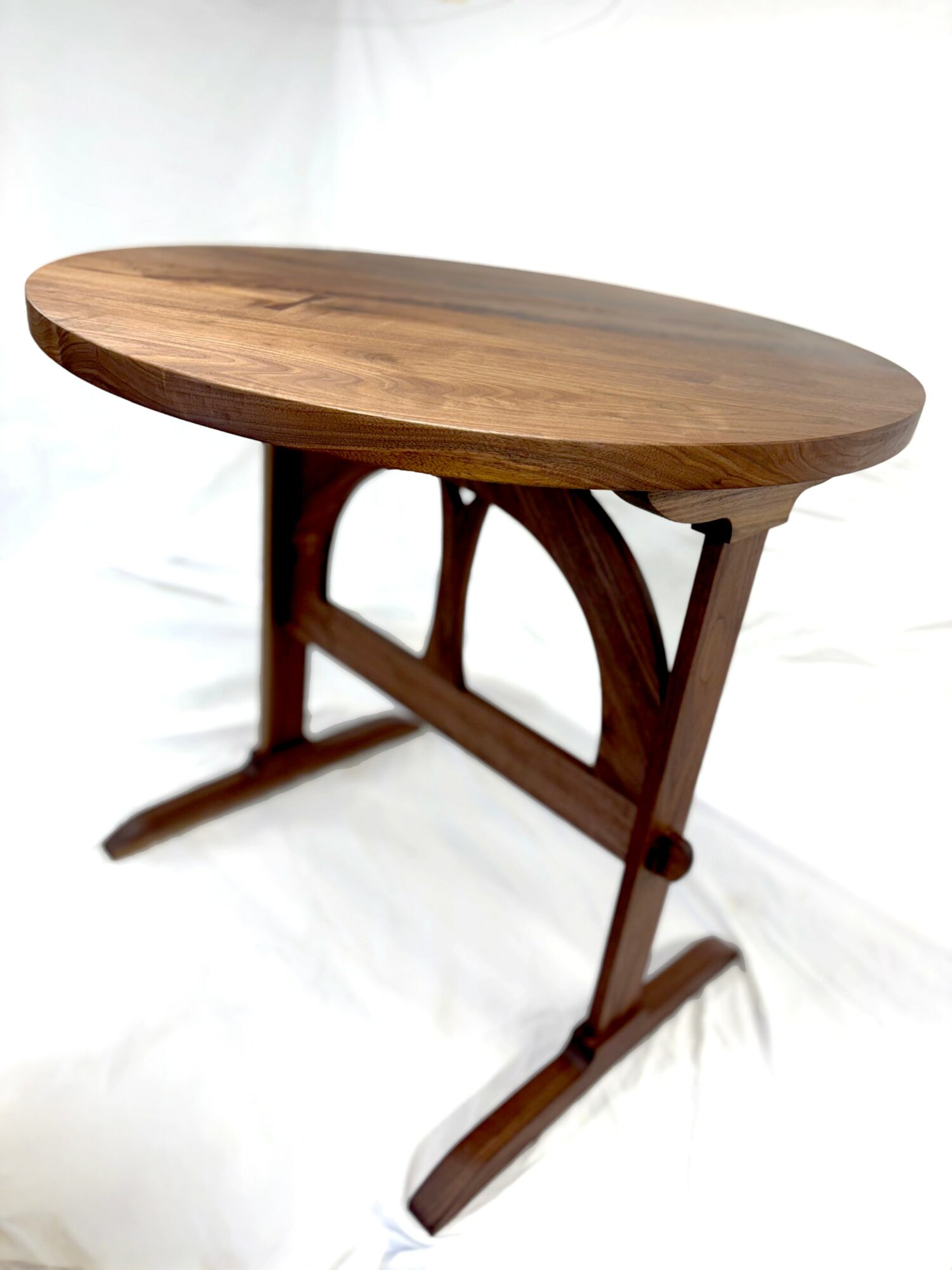 Wooden oval table with curved legs and support structure, viewed from the side, against a plain background.