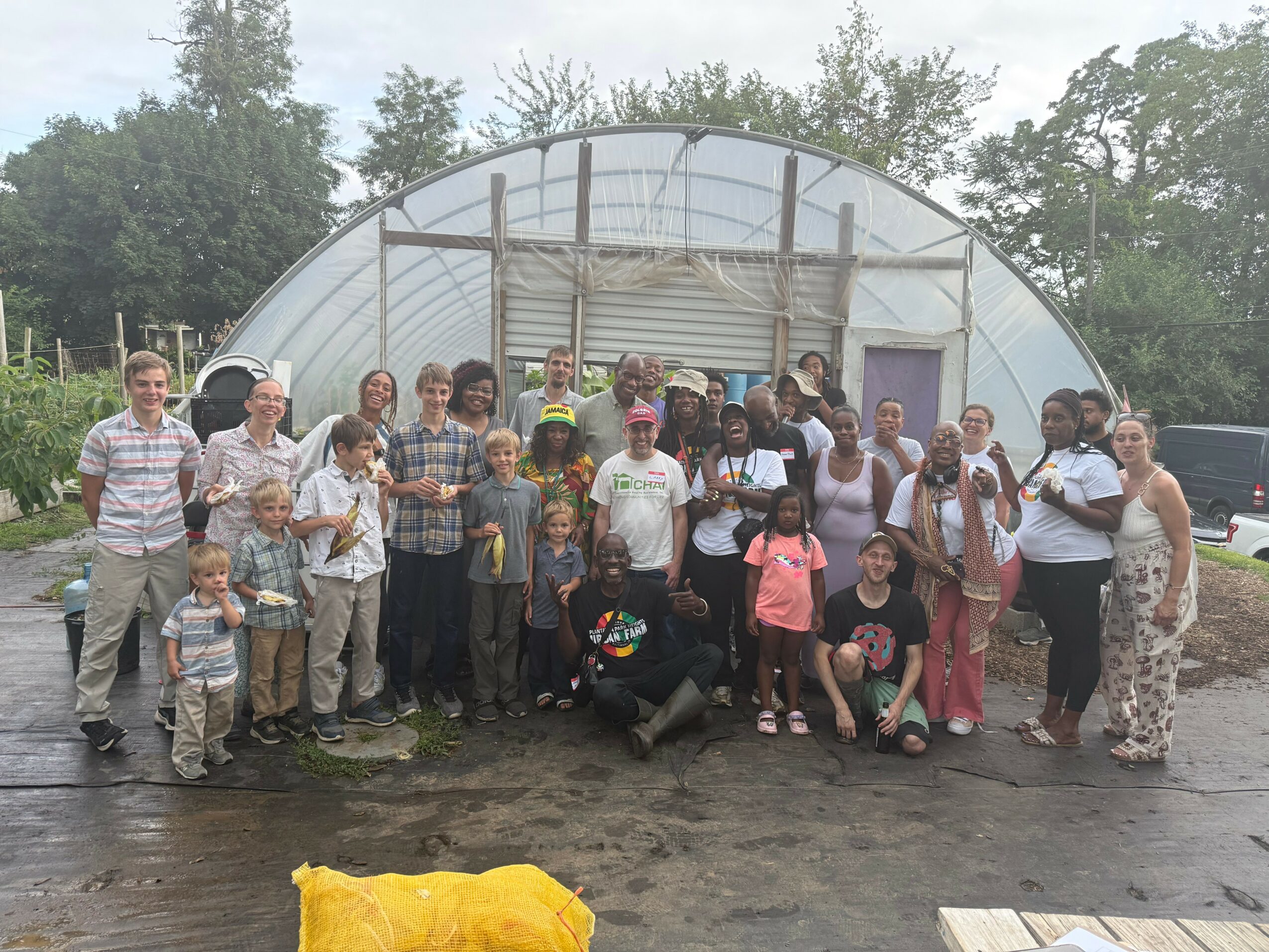Group of people, including children and adults, standing outside a greenhouse on a cloudy day.