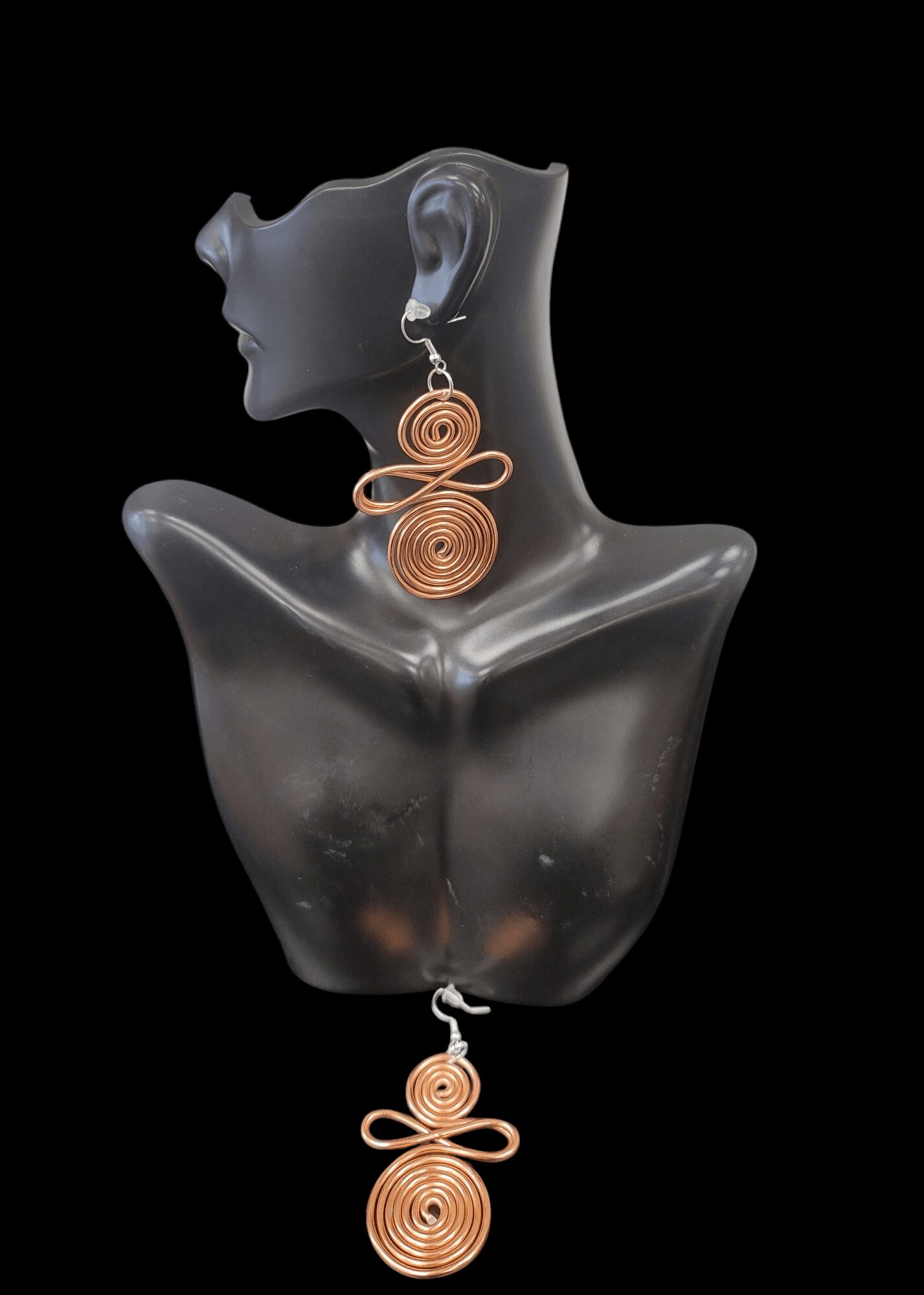 Display of a mannequin bust with matching spiral earrings and pendant, all made of copper wire, against a black background.