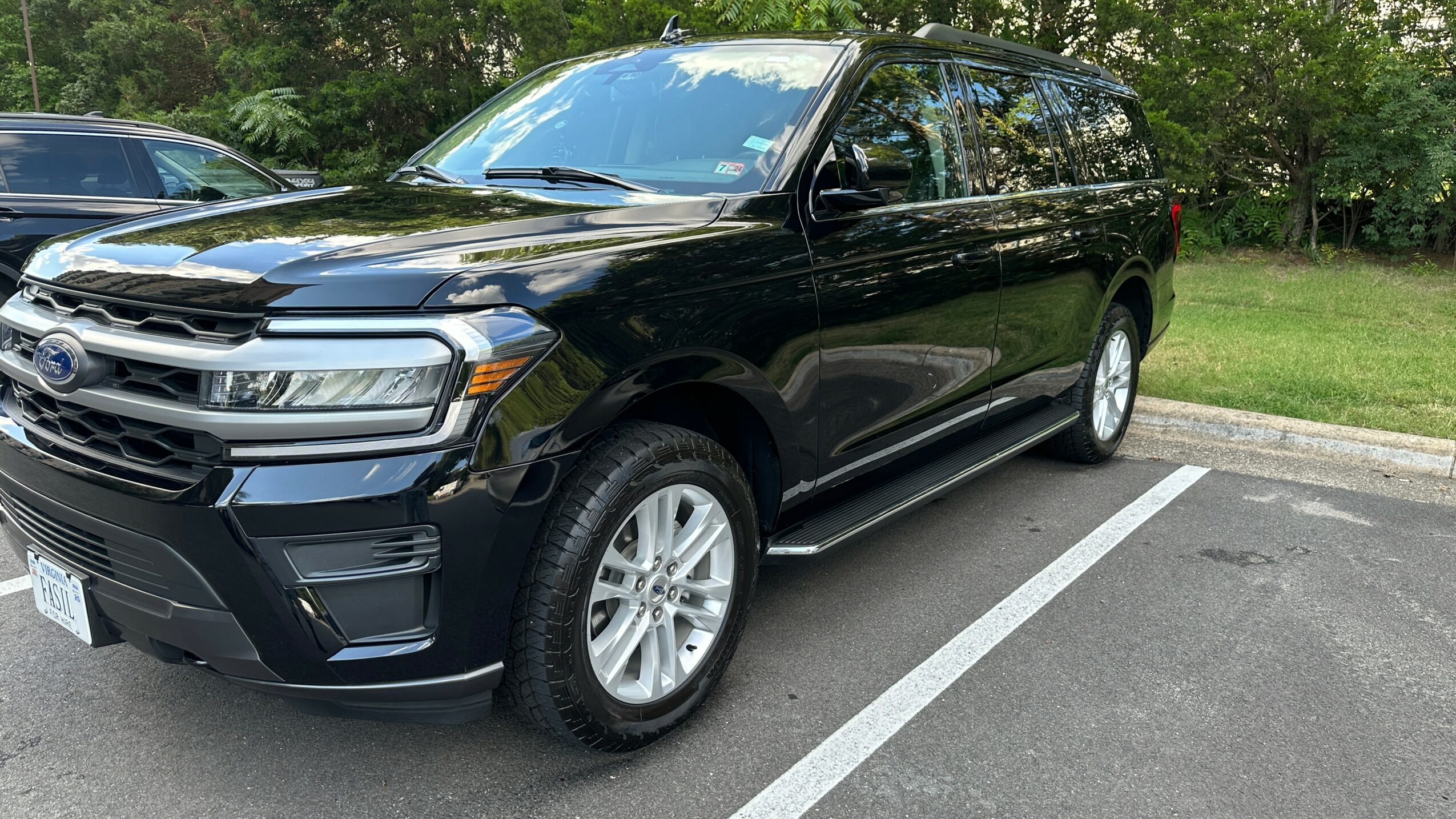 Black SUV parked in a parking lot with trees in the background, front and side view, shiny surface, clear weather