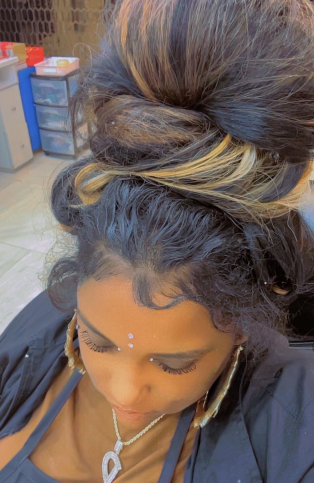 Top view of a woman with styled hair, jewelry, and decorative face dots, looking downward.