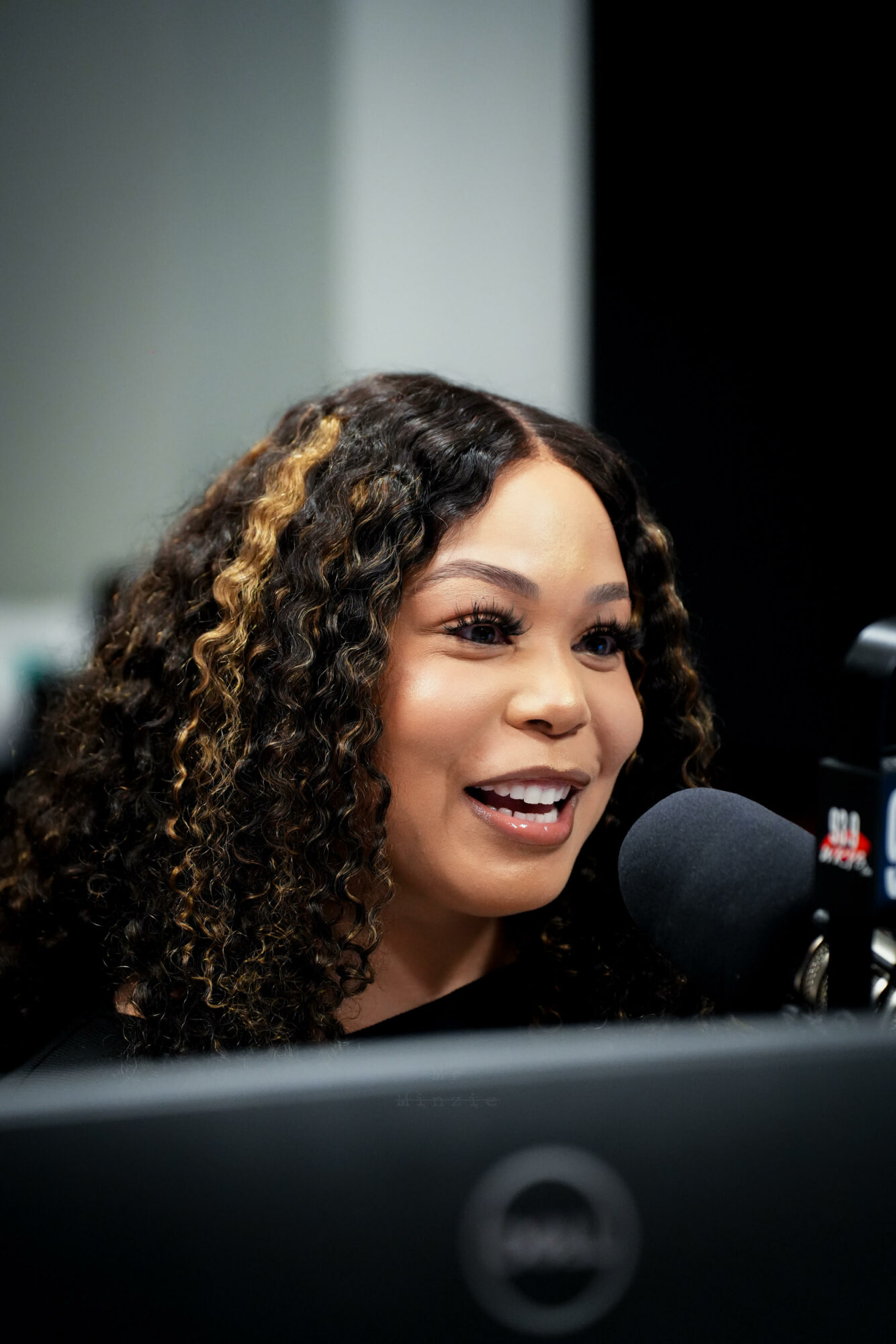 Woman with curly hair speaking into a microphone in a studio setting.
