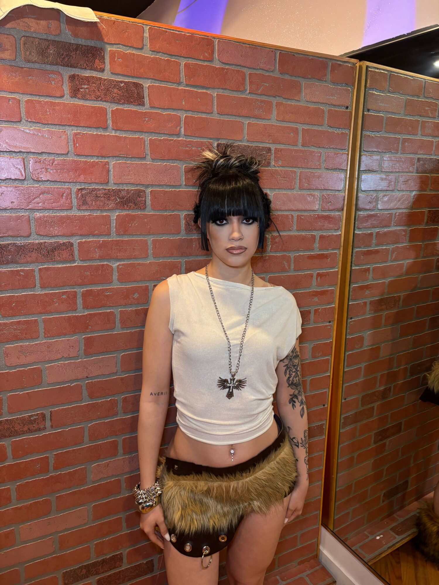 Young woman with dark hair and bangs, wearing a white top, shorts, and jewelry, lying on a brick floor.