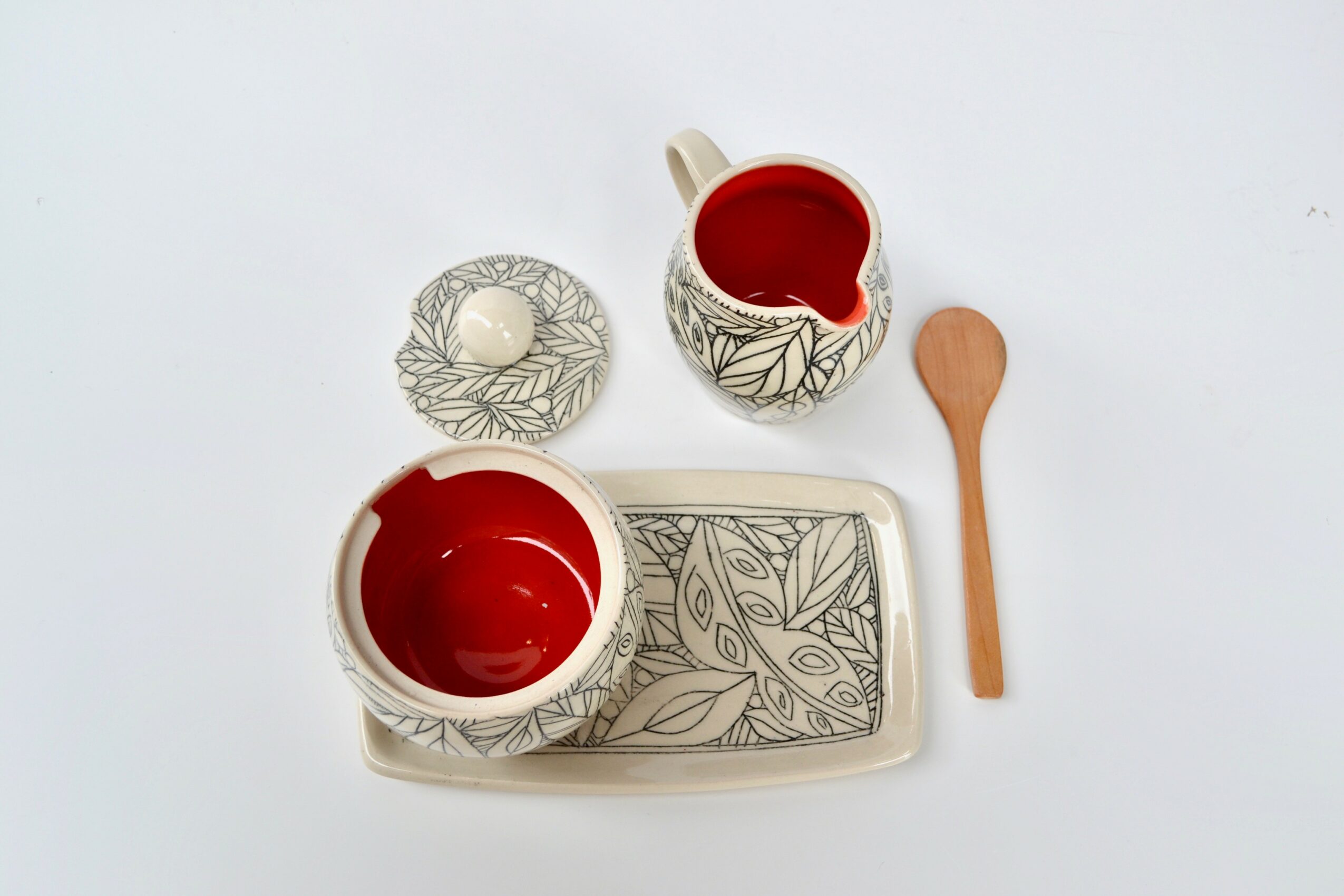 Tea set with a teapot, cup, spoon, and tray, all with leaf patterns, on a white background.