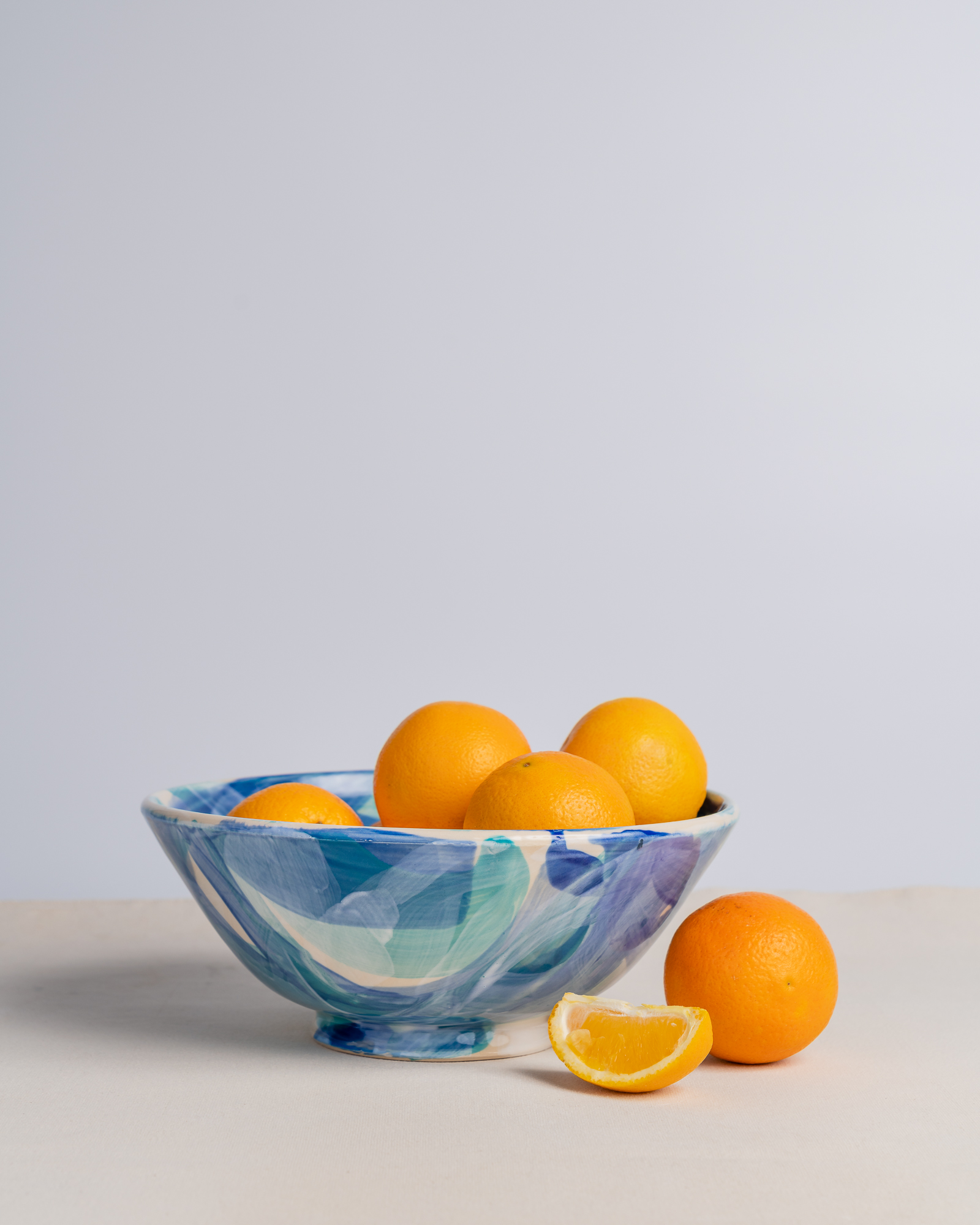 A glass bowl with oranges and lemon slices on a light surface against a plain background.