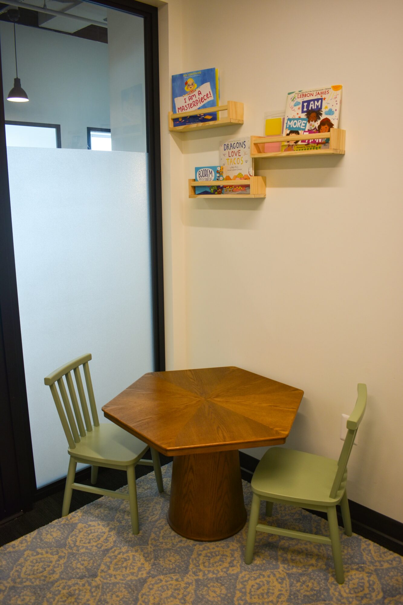 Small table with two chairs in a corner, shelves with books on the wall, frosted glass door nearby.