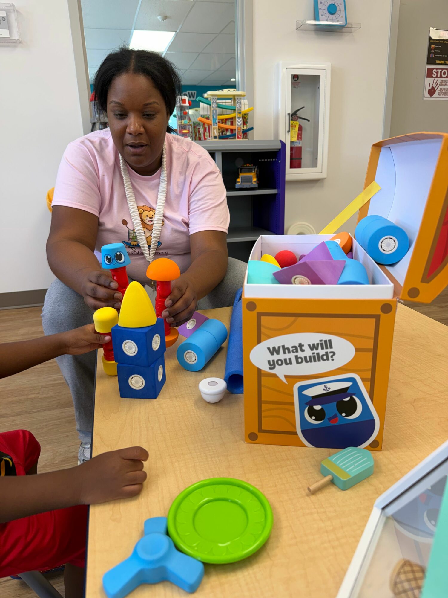 Child playing with colorful toys on a table, with a box labeled 'Your Friendly Robot Guide' nearby.