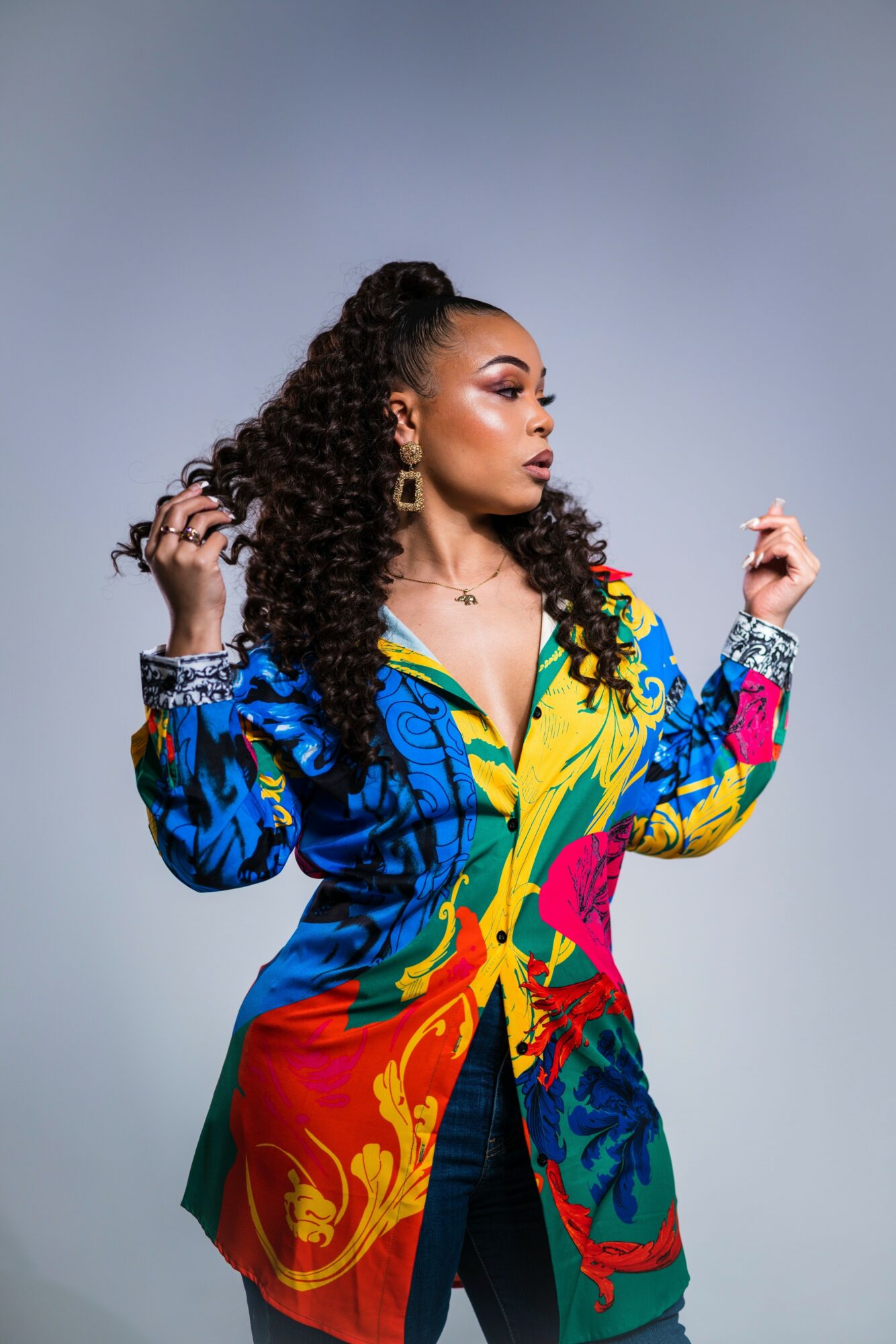 Woman with curly hair in a colorful patterned jacket, looking to the side, against a plain background.