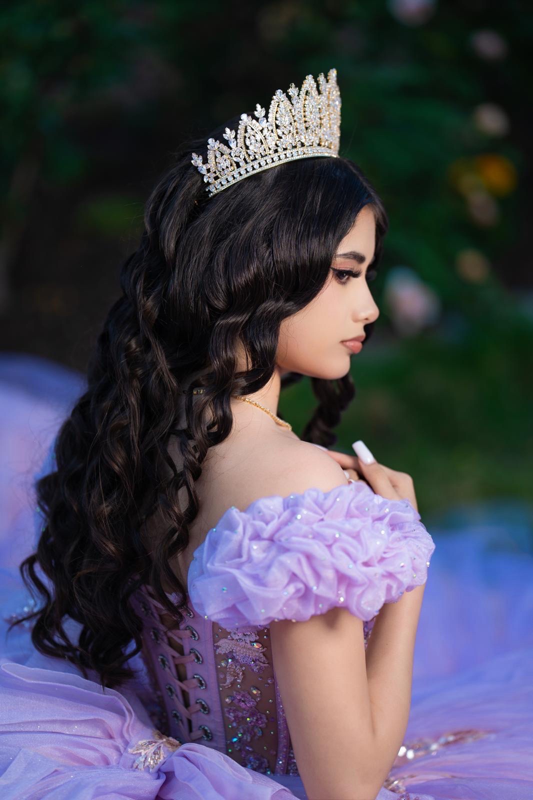 Profile of a young woman wearing a crown and a lavender dress with ruffled sleeves, outdoors with greenery.