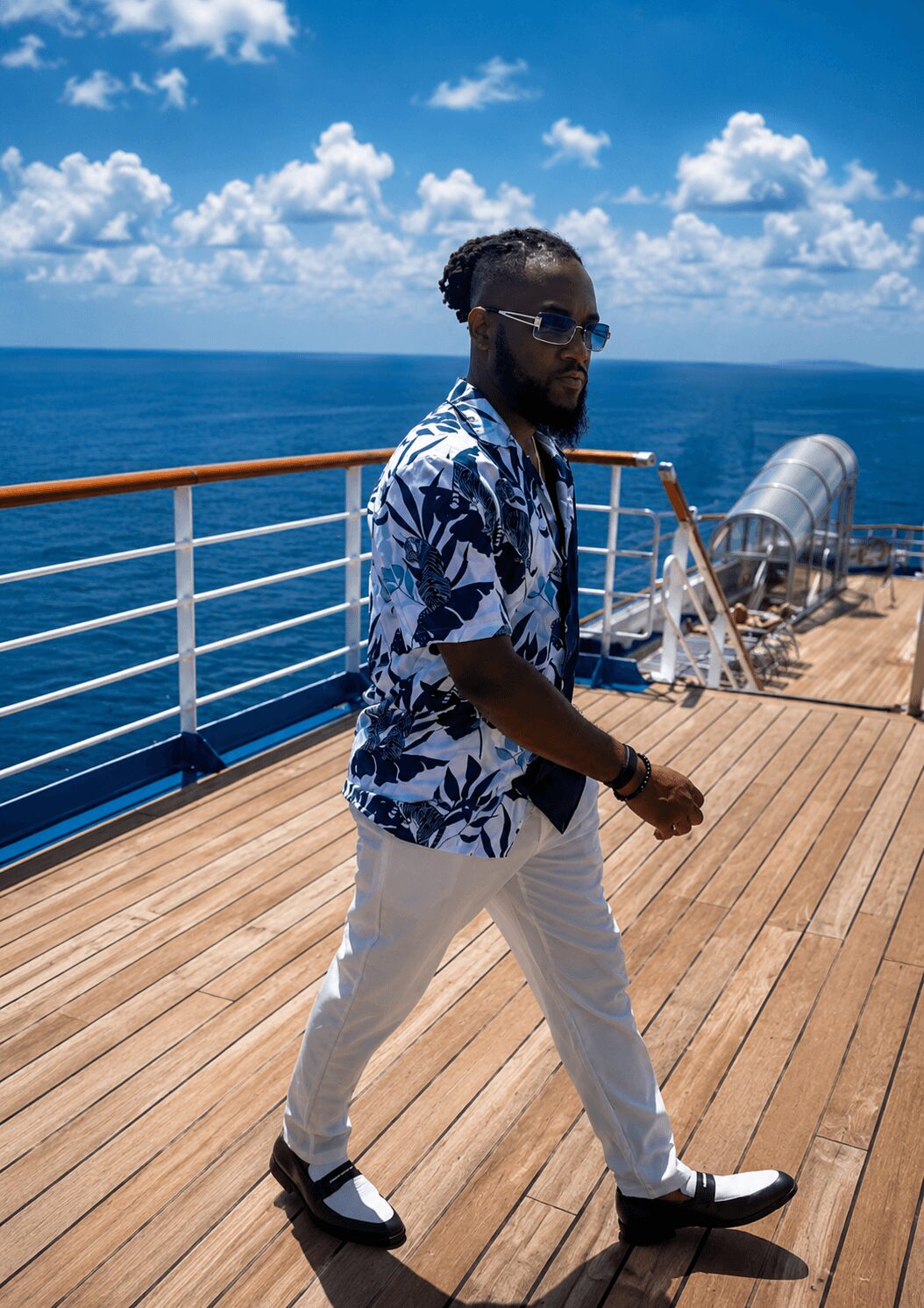 Man walking on a ship deck with ocean and sky in background, wearing sunglasses, floral shirt, and white pants.
