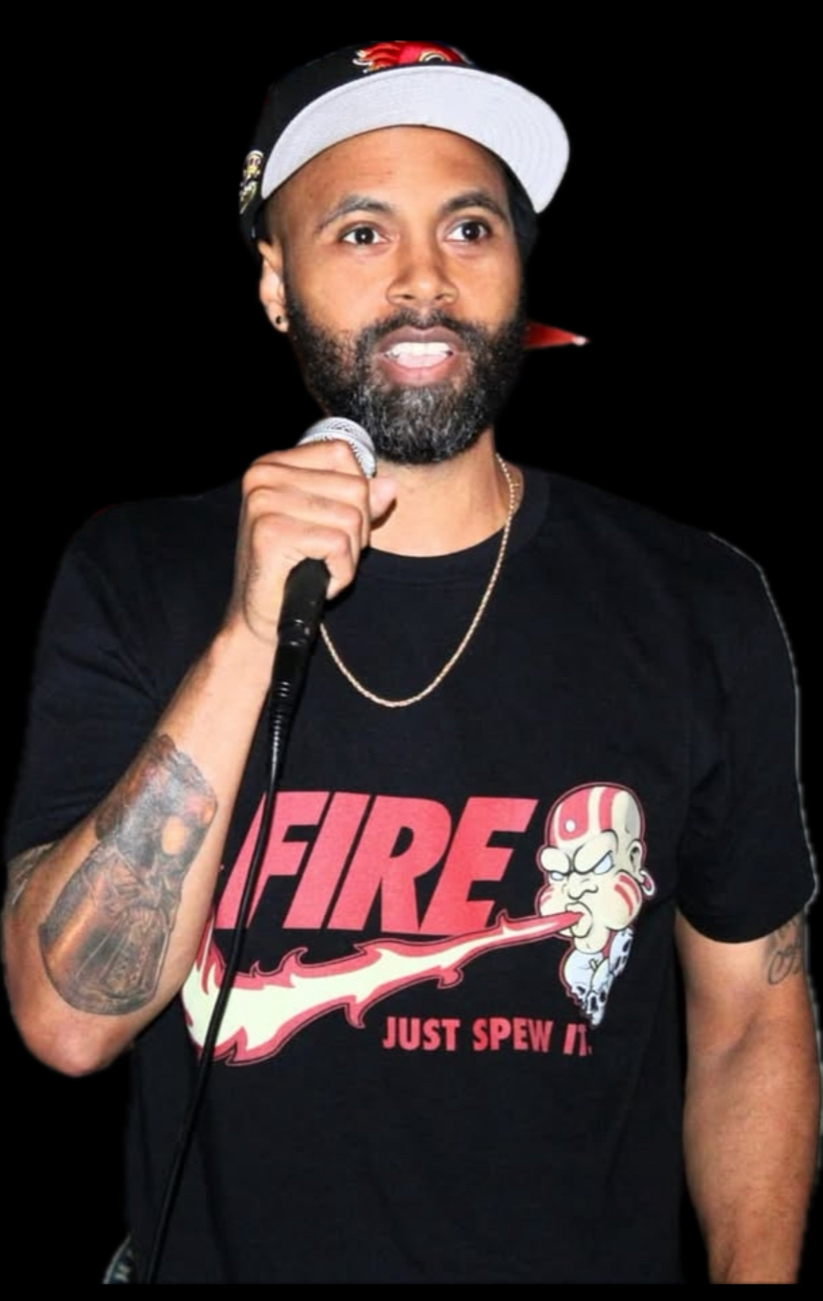 Person with beard and tattoos holding a microphone, wearing a black T-shirt and a white cap with a red logo, smiling.