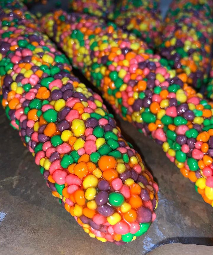 Close-up of colorful candy-coated chocolate sprinkles on a surface, showing vibrant pink, yellow, green, purple, and orange colors.