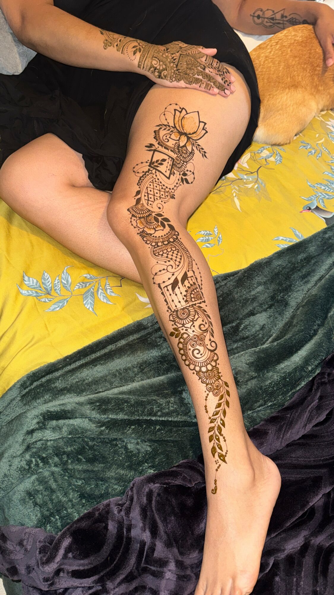 Person with a detailed snake tattoo on leg, lying on a bed with yellow and green bedding, hand resting on thigh.