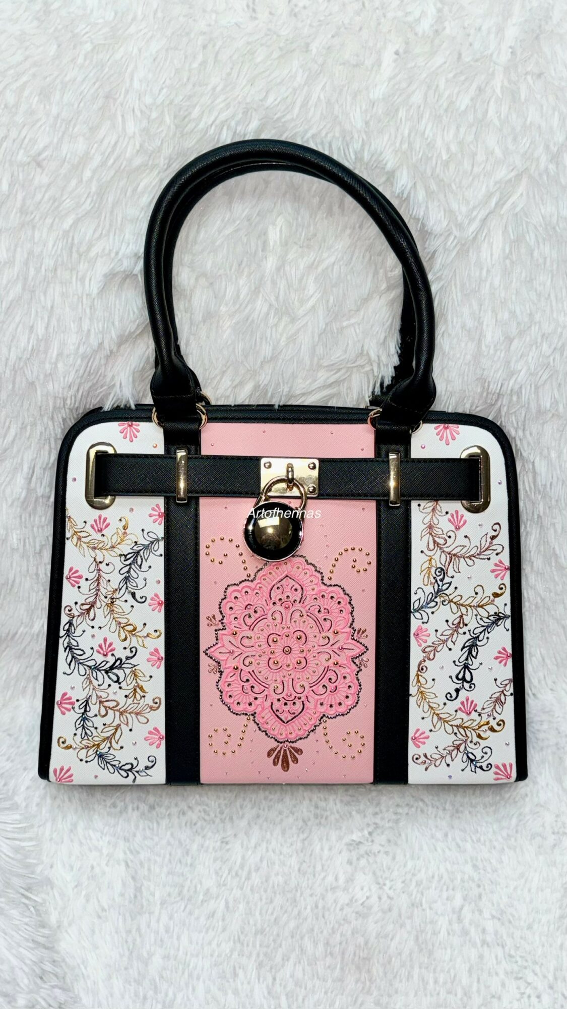 Handbag with black handles, pink and white design, floral pattern, and a hanging decorative element.