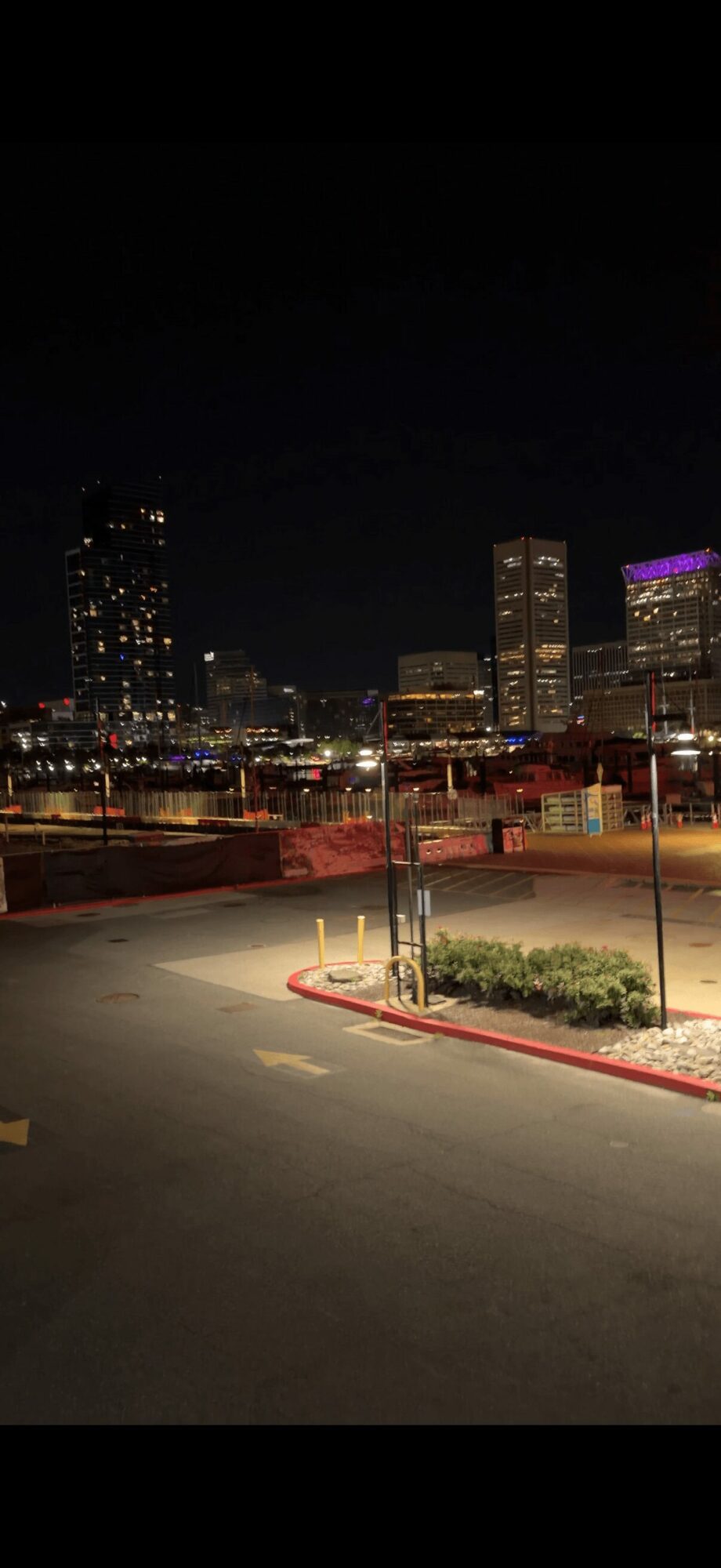 Night cityscape with buildings, street, and parking lot, illuminated by city lights.