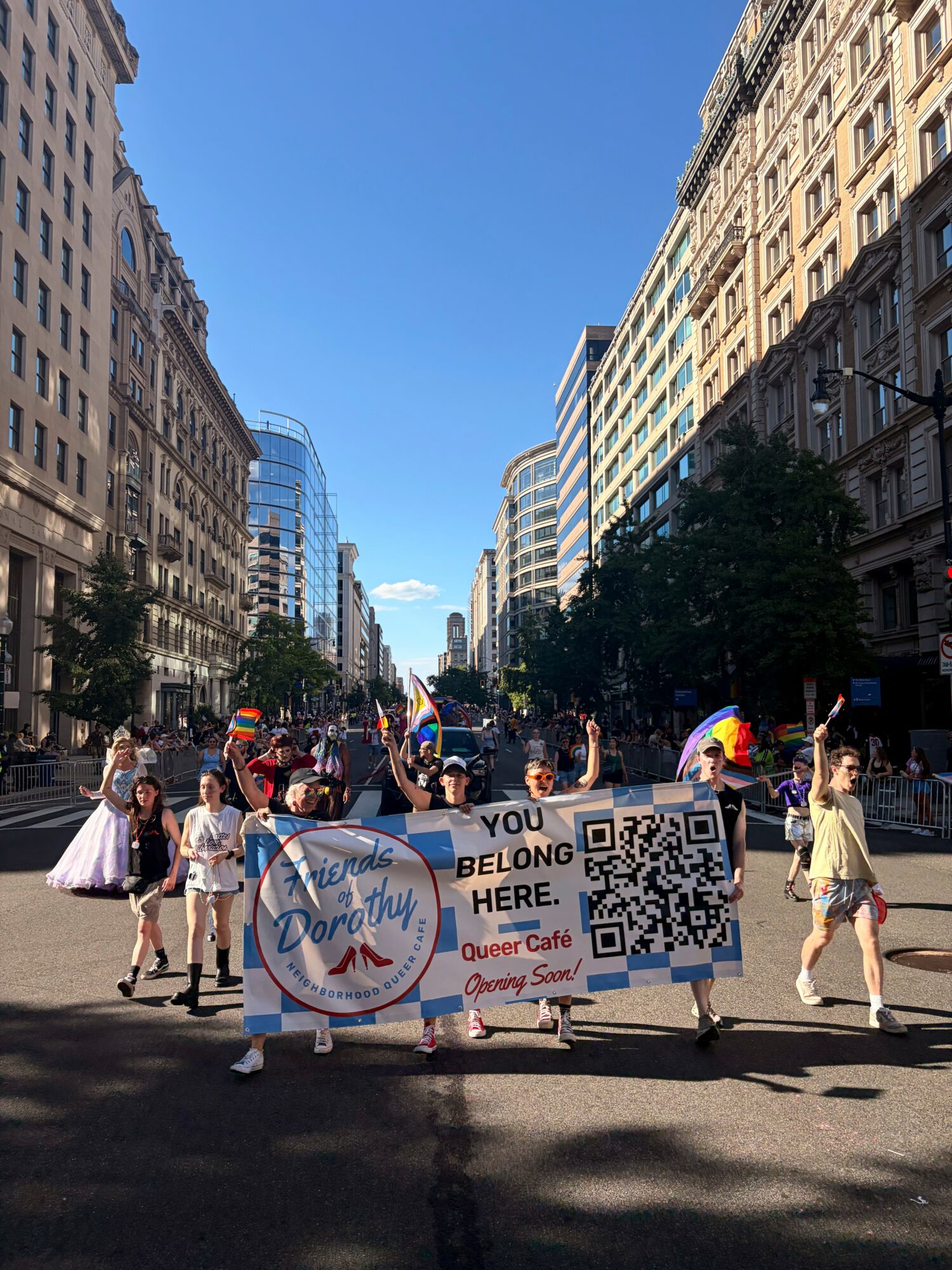 People holding a banner and flags in a city street with tall buildings and trees, sunny day.
