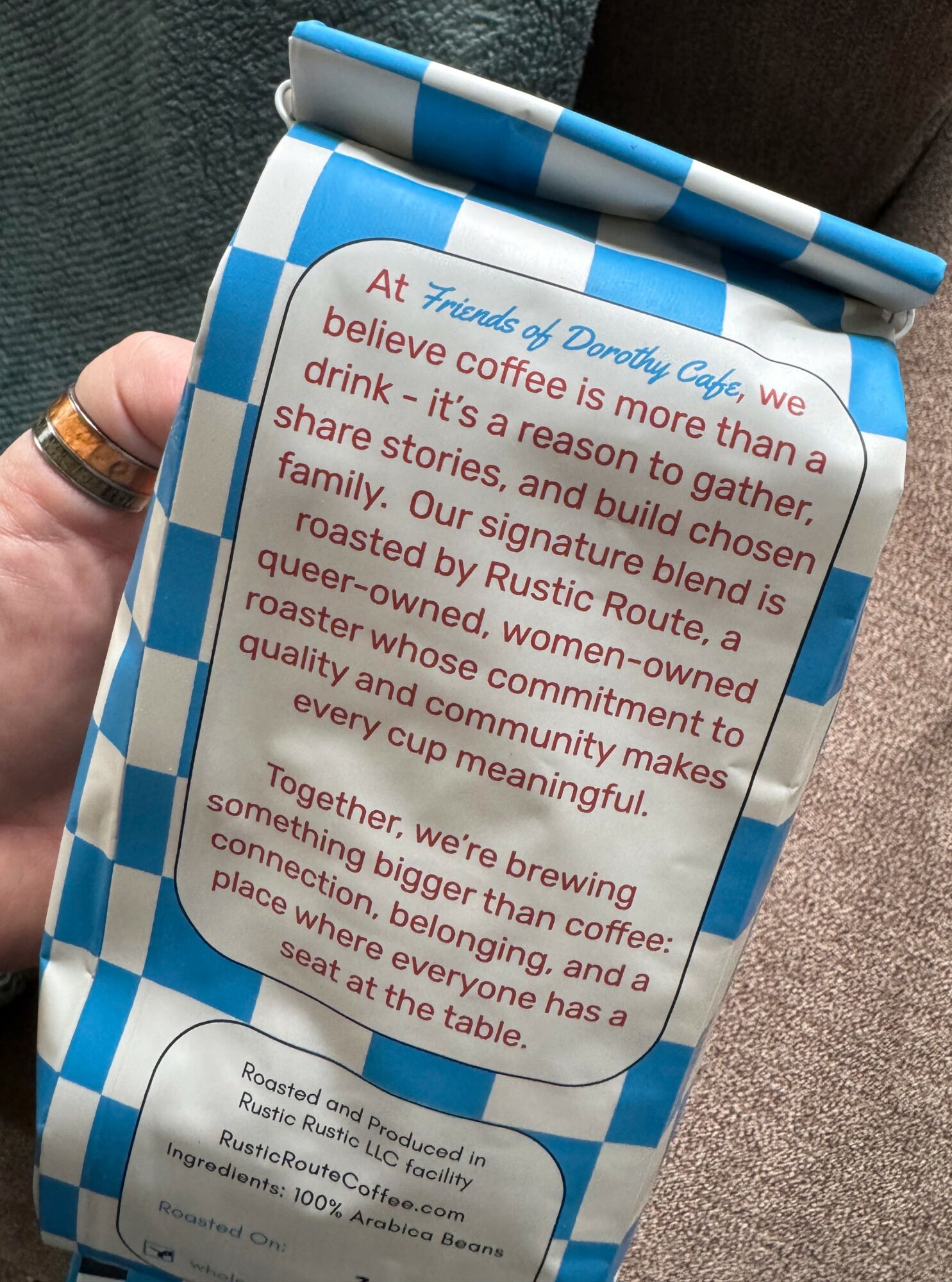 A blue and white checkered coffee cup sleeve with text about coffee and community, held by a hand.