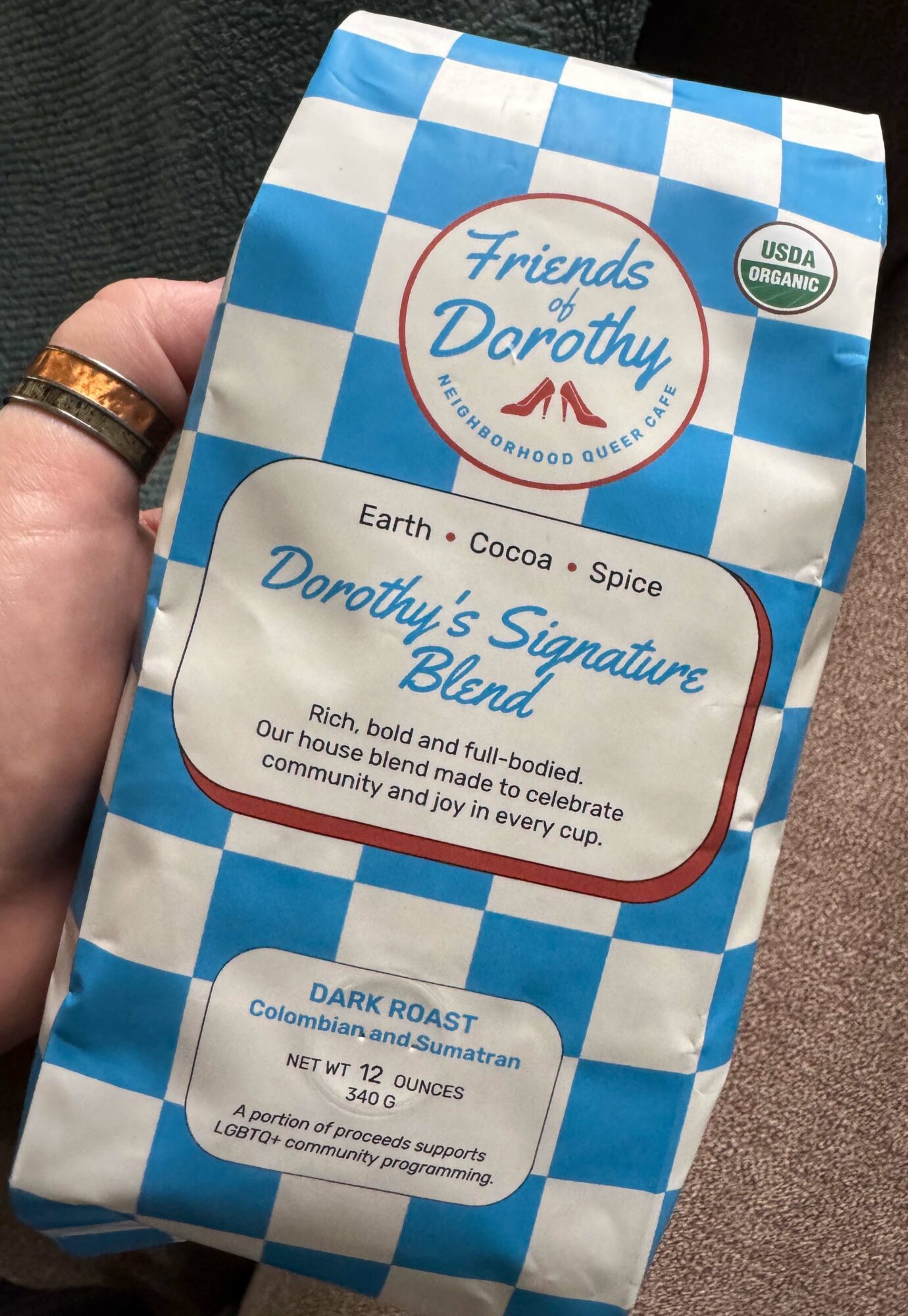 Hand holding a blue and white checkered bag with a circular logo and text about Dorothy's signature blend coffee.