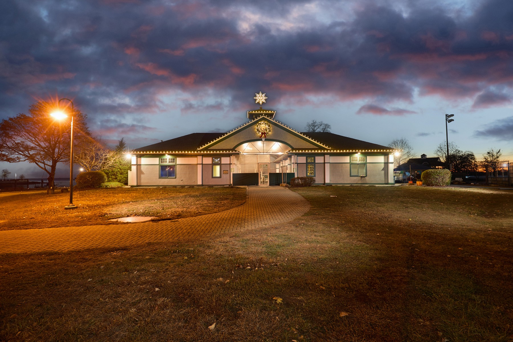 Building with illuminated entrance, dark sky with clouds, and surrounding area at dusk.