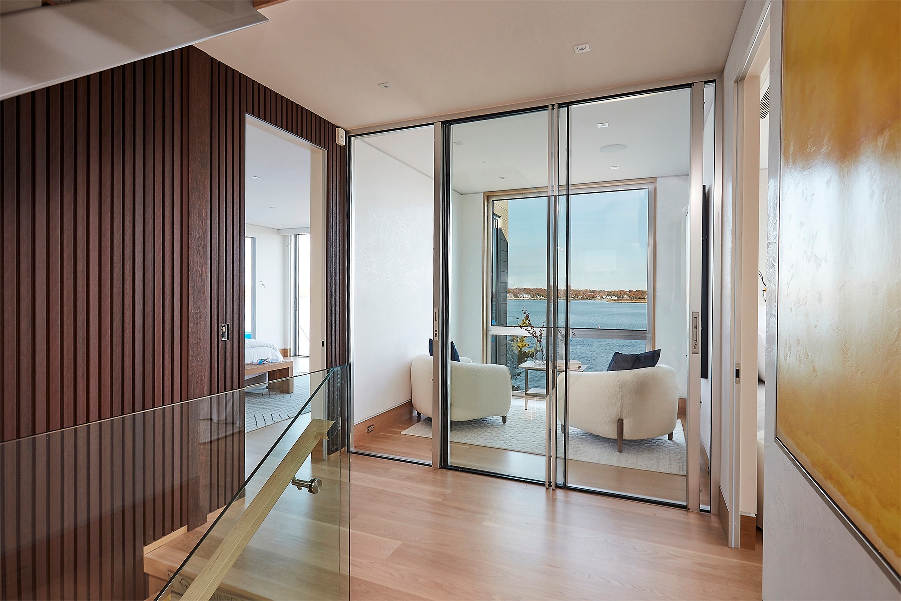 Living room with glass sliding doors leading to balcony, two white chairs, and a view of water outside.