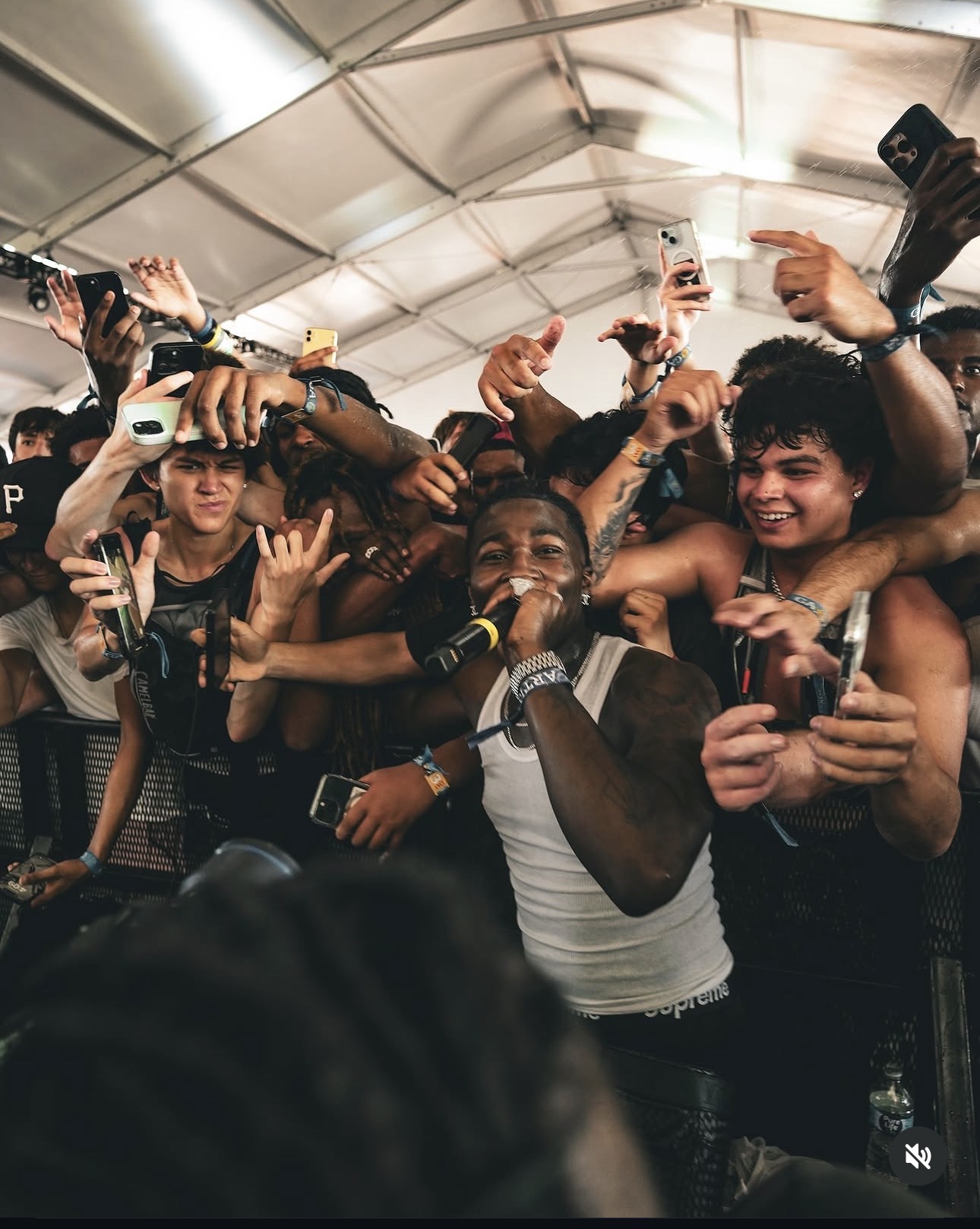 A group of people, mostly young, are gathered in a tent, smiling and taking photos with a performer in the center.