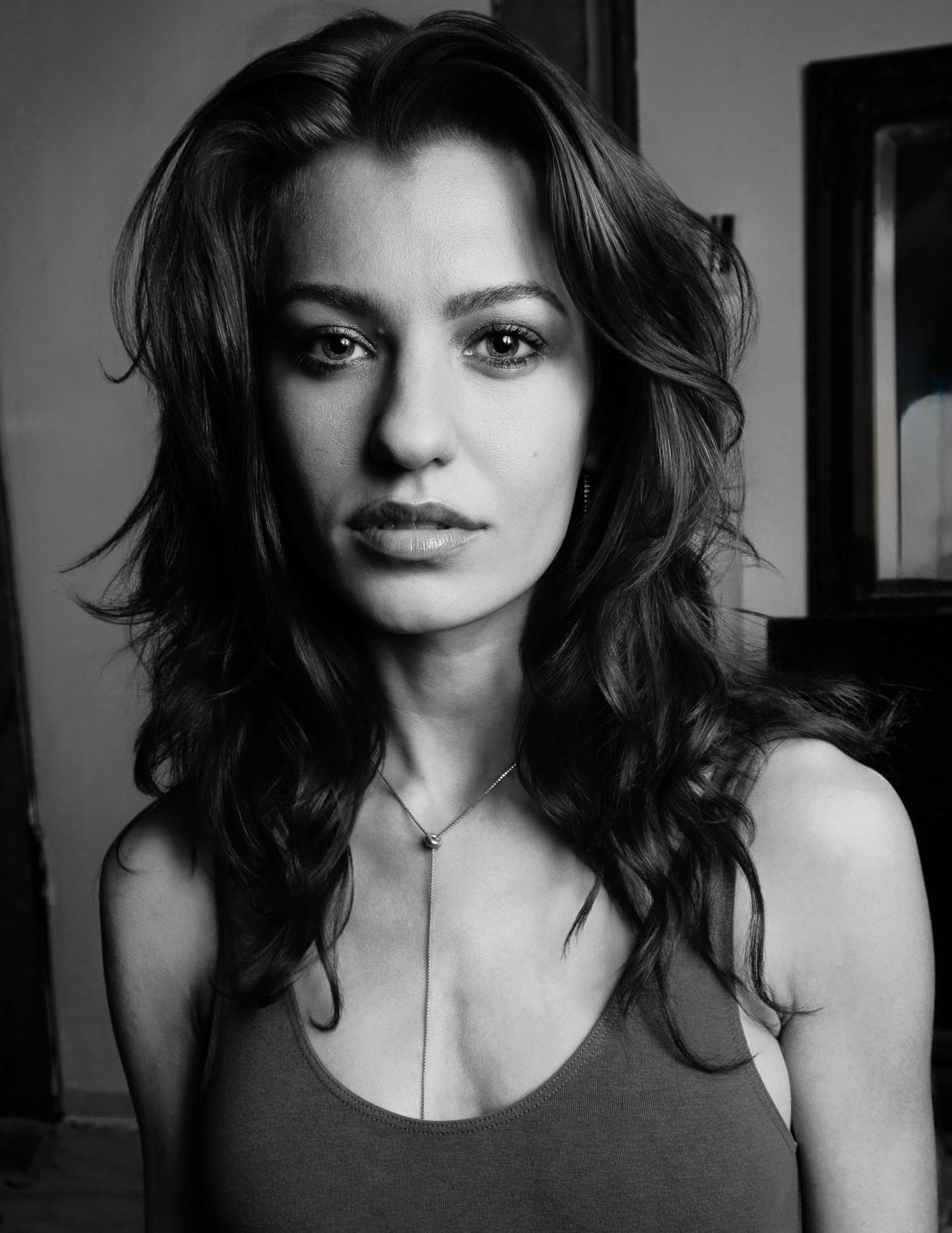 Black and white portrait of a woman with wavy hair, looking directly at the camera, wearing a tank top and necklace.