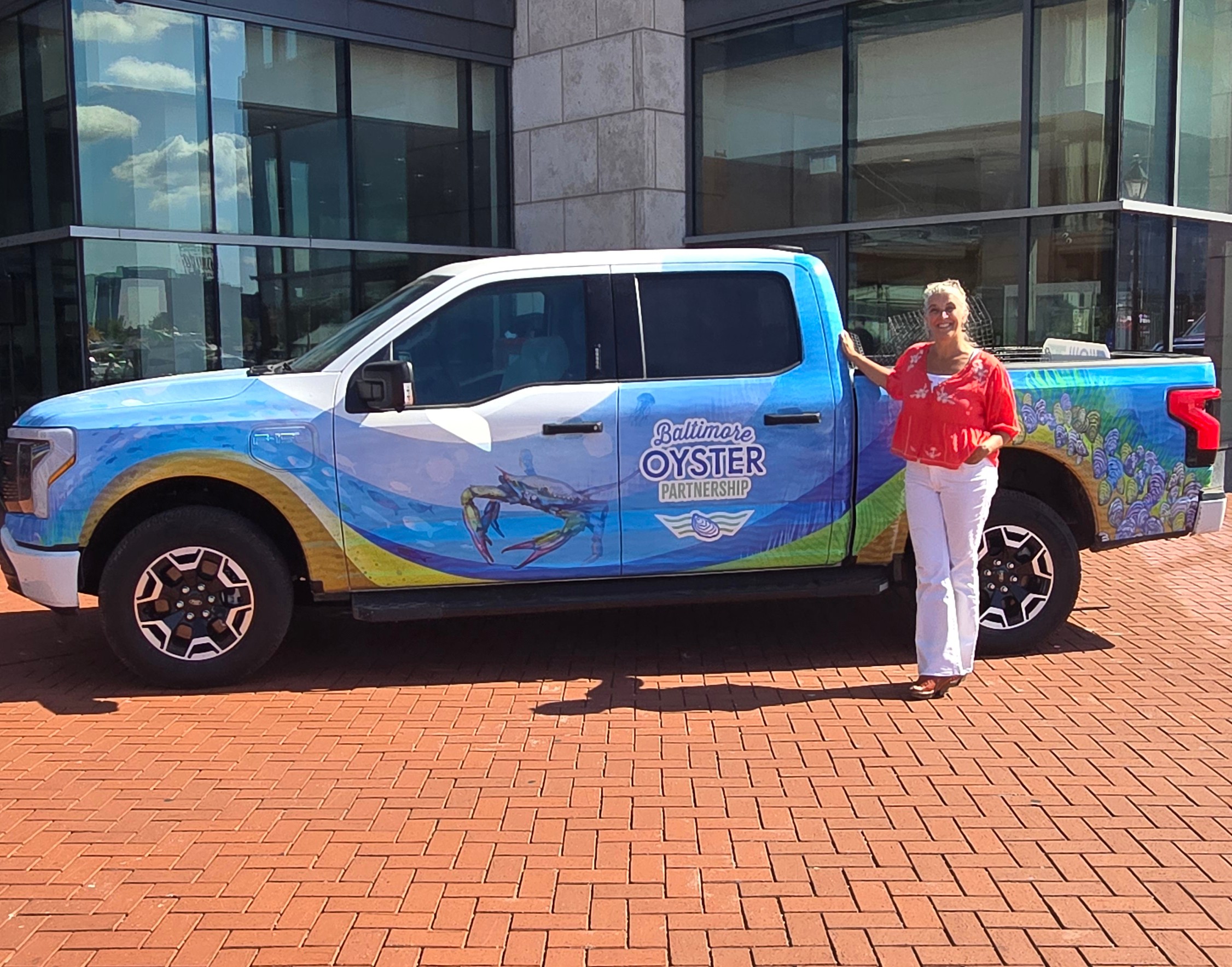 Person standing next to a colorful truck with a large oyster graphic and text, in front of a modern building.