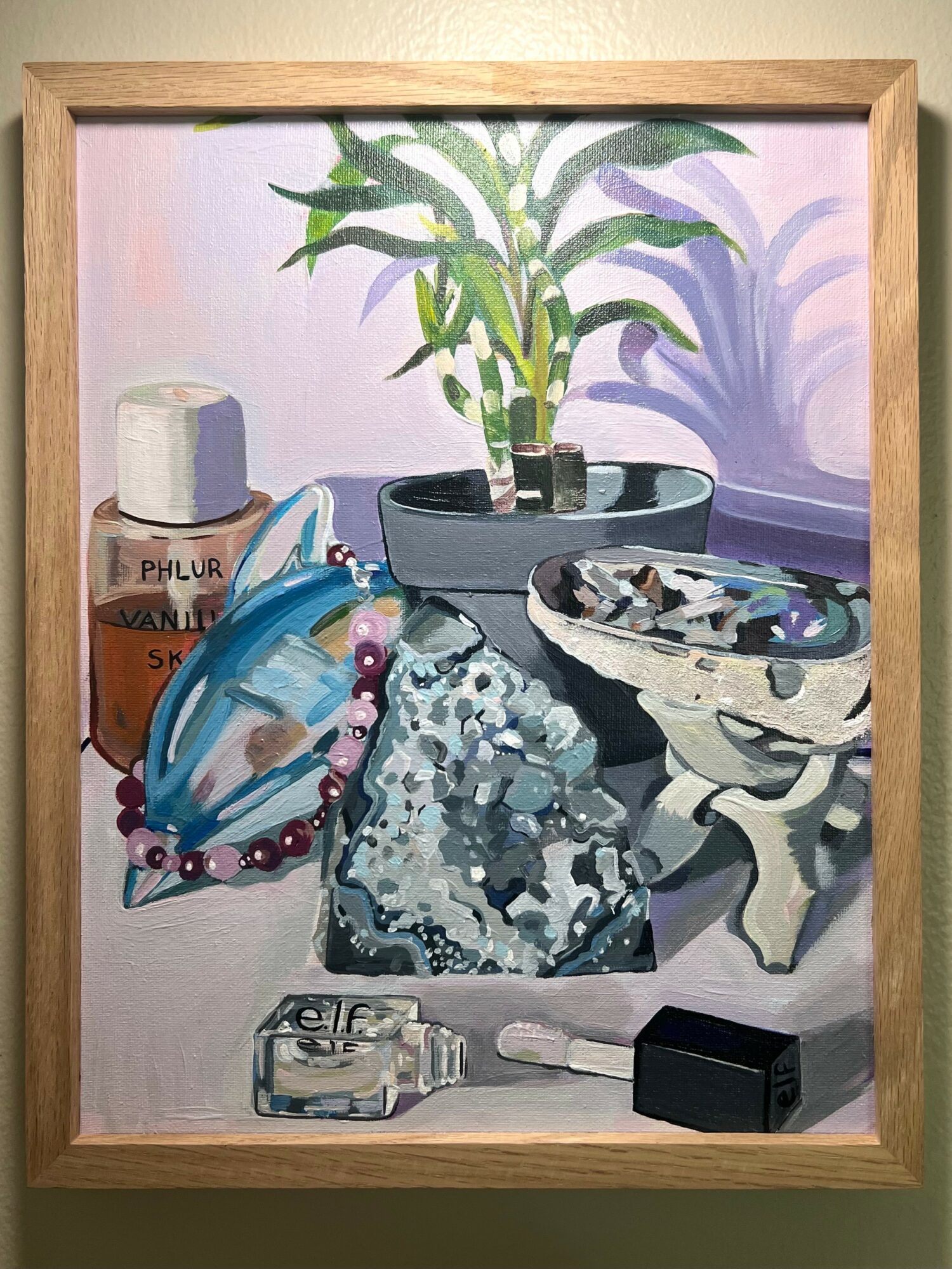 Still life with a potted plant, jewelry, a bottle, and various objects on a table, framed in wood.