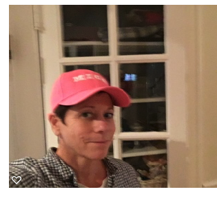 Person wearing a pink cap and checkered shirt, standing indoors near a window with multiple panes.