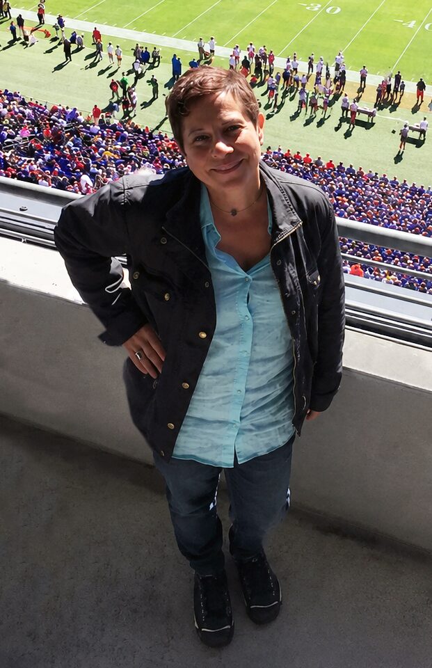 Woman standing on balcony overlooking a sports stadium with spectators and players on the field.
