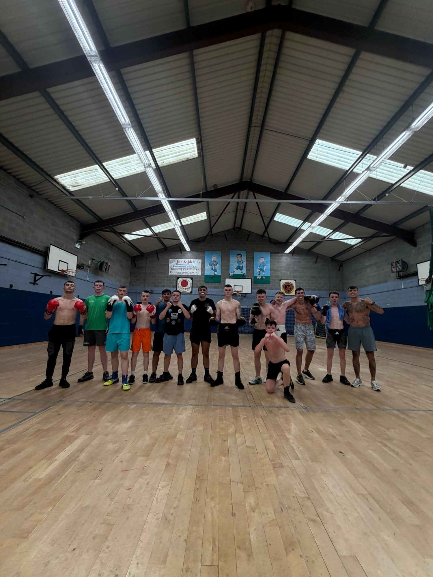 Group of people standing in a gymnasium with a wooden floor and high ceiling, some holding papers or objects.