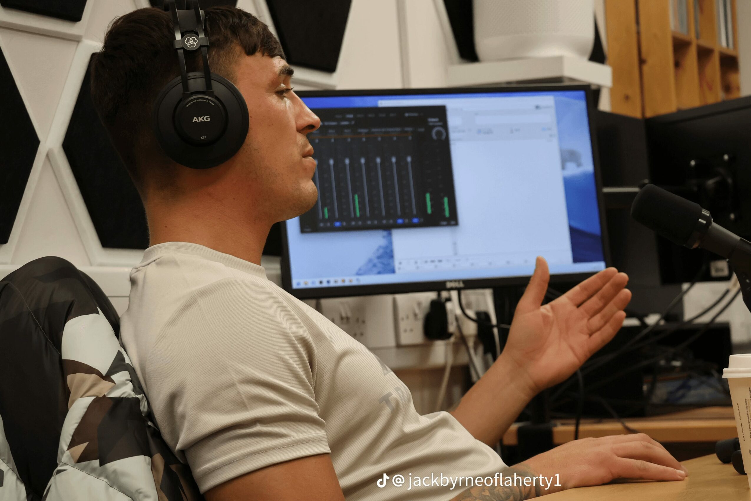 Young man wearing headphones working at a computer with audio editing software, gesturing with his hand, in a studio.