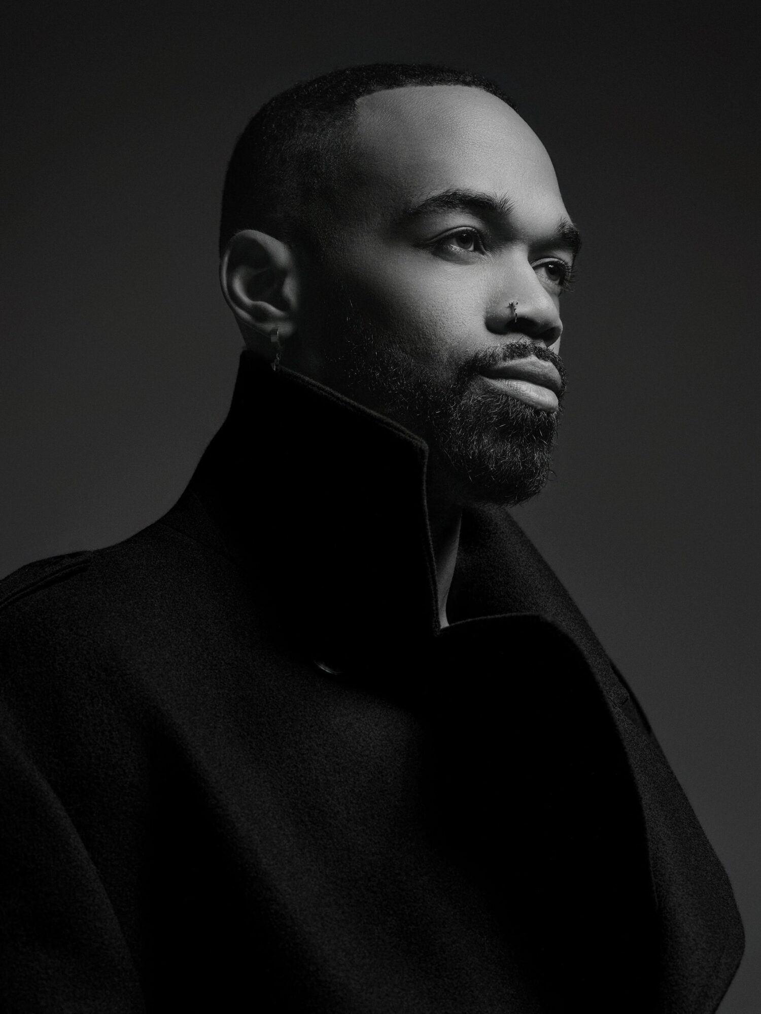 Portrait of a man with a beard and short hair, wearing a dark coat, looking to the right, in black and white.