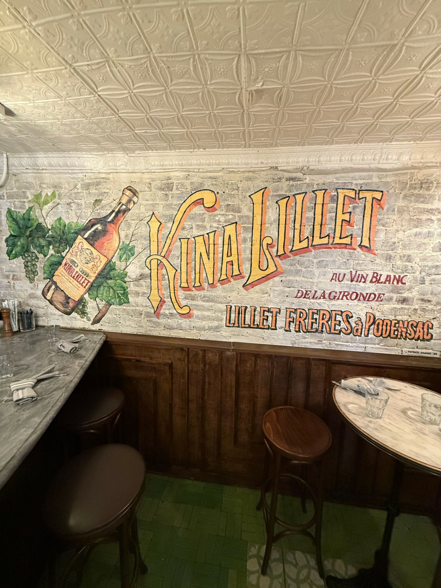 Vintage sign with a bottle illustration, text, and decorative elements, mounted on a wall with a wooden panel below.