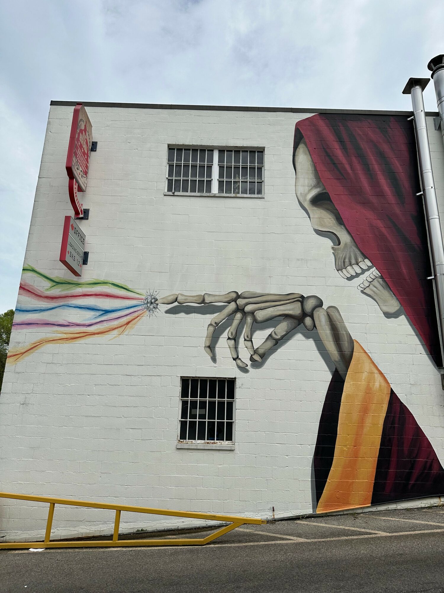 Mural of a hand holding colorful ribbons on a white wall with windows and a ladder nearby.