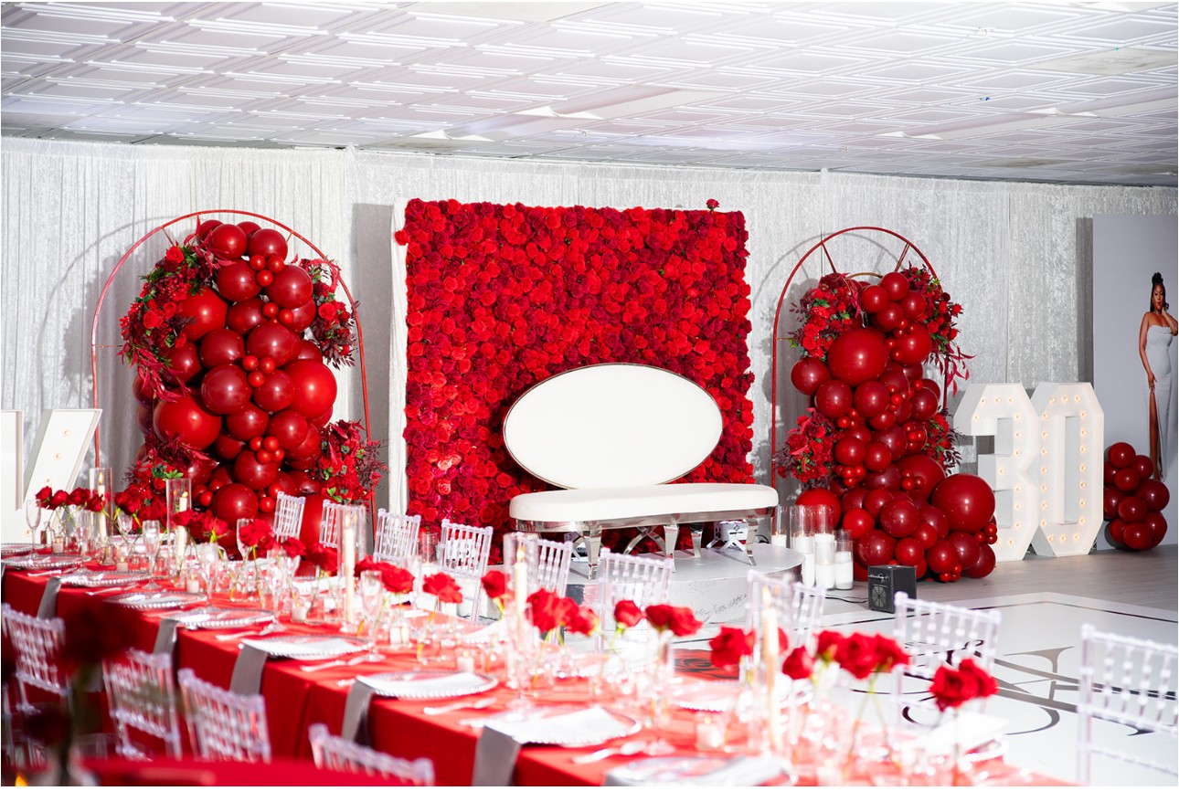 Decorated event space with red balloons, floral backdrop, and a long table set for a celebration.