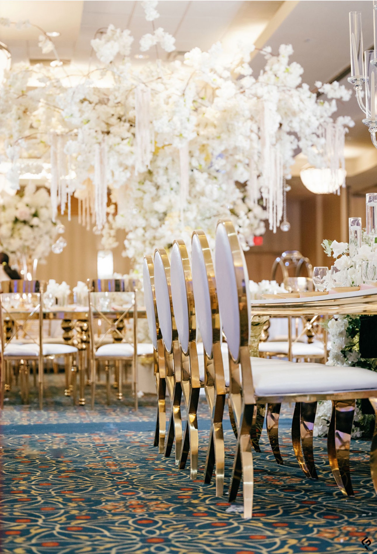 Elegant banquet table with white floral centerpieces and gold chairs in a decorated event space.