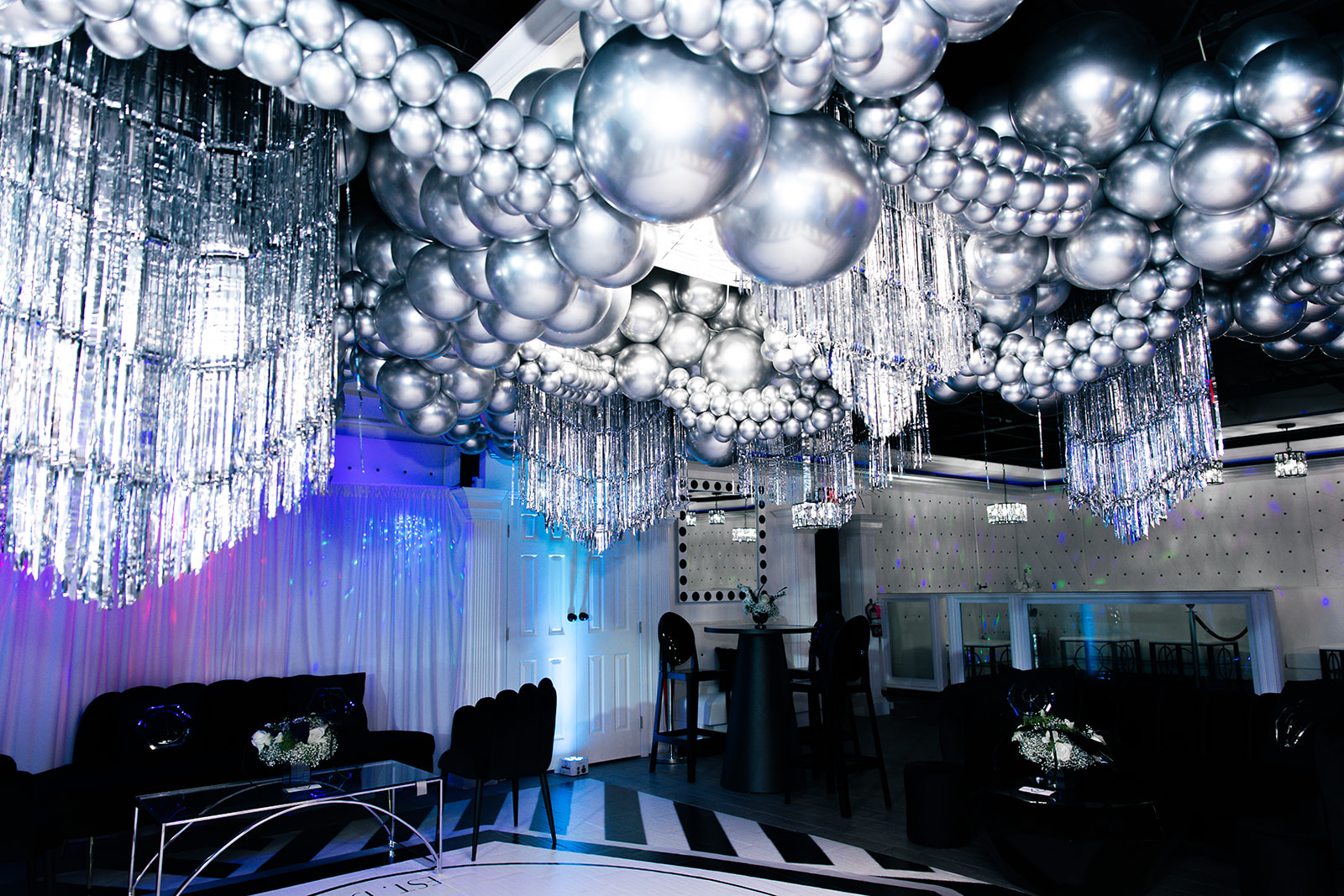 Decorative ceiling with silver balloons and hanging crystal-like ornaments in a dimly lit event space.