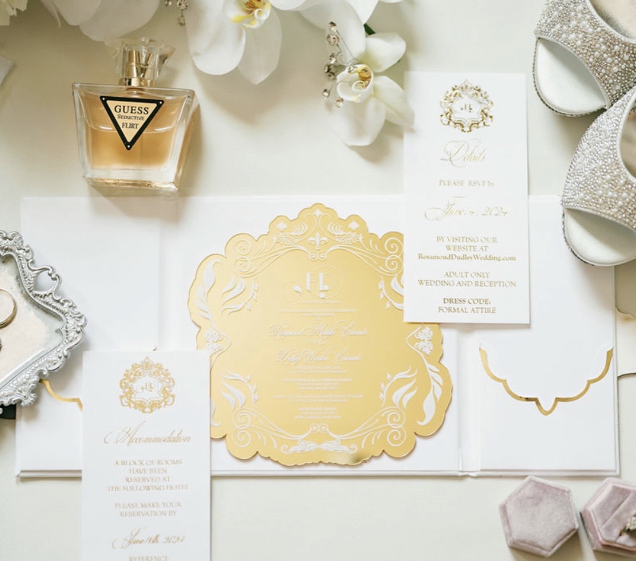 Wedding invitation suite with gold and white details, surrounded by perfume, shoes, and decorative items.