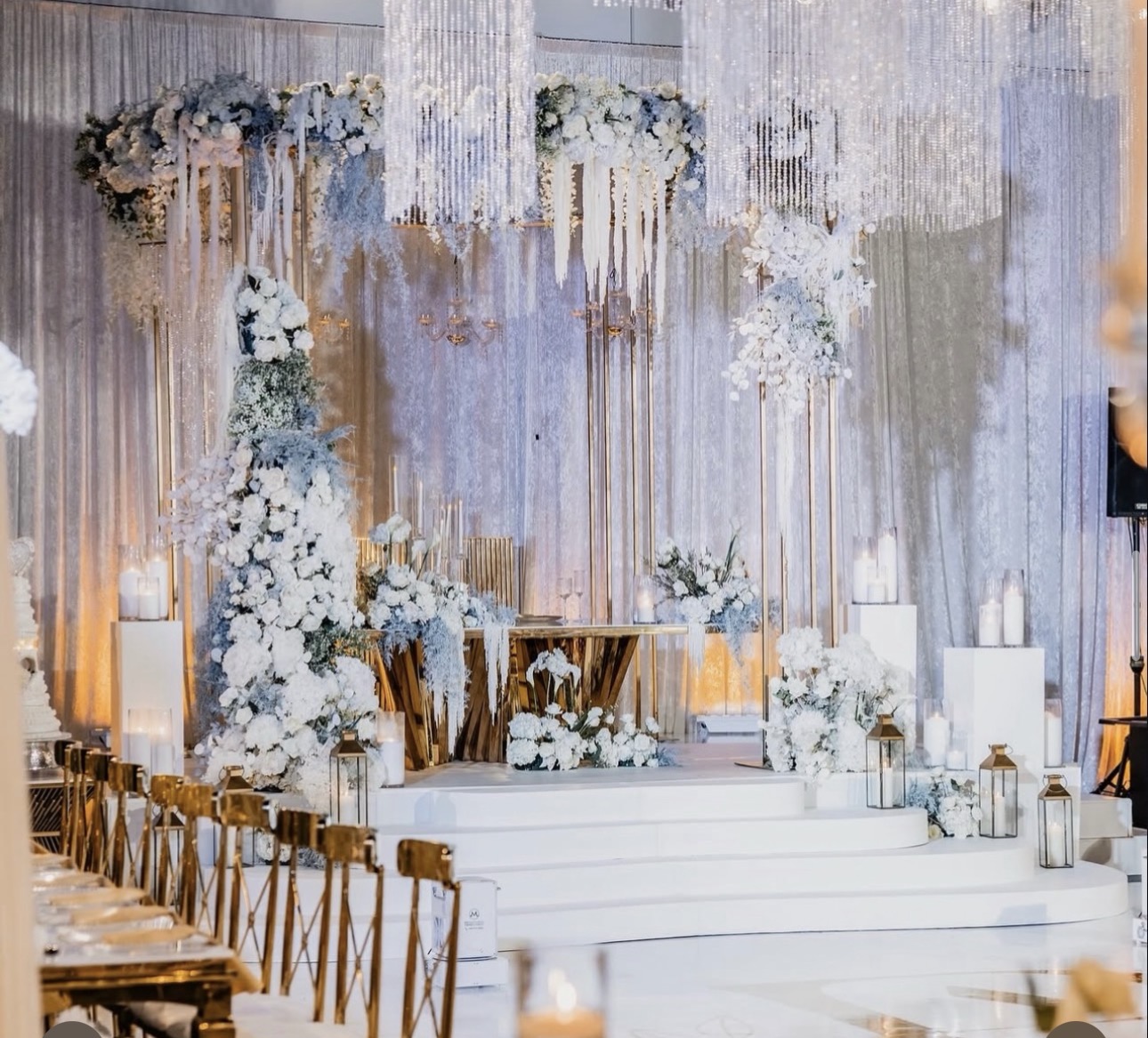 Elegant wedding stage decorated with white flowers, candles, and drapes, with chairs arranged in front.