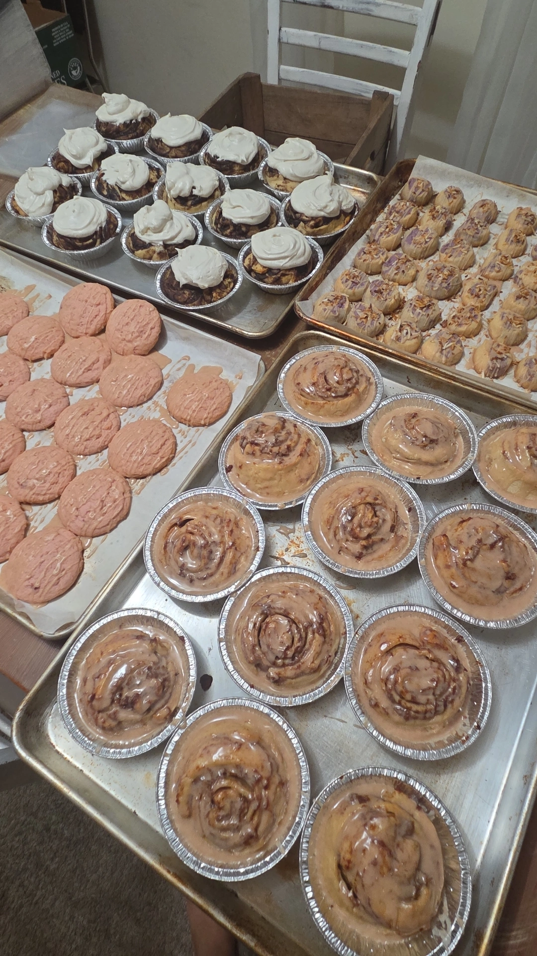 Assorted baked goods including cupcakes, cookies, and muffins on trays in a kitchen setting.